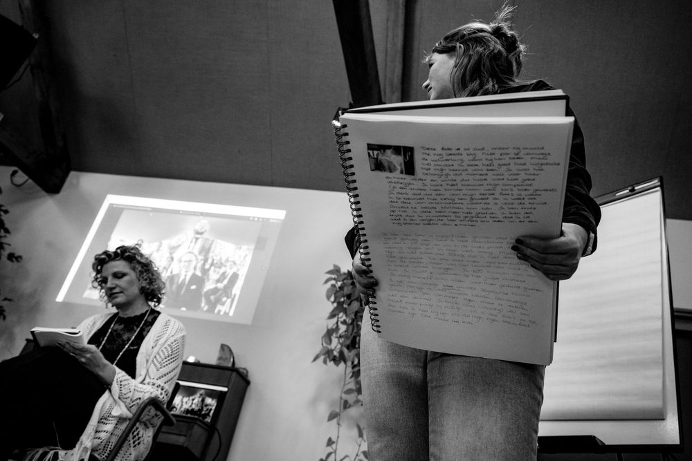 Black and white photo of two women, one reading a book and another holding an open notebook at an indoor presentation.