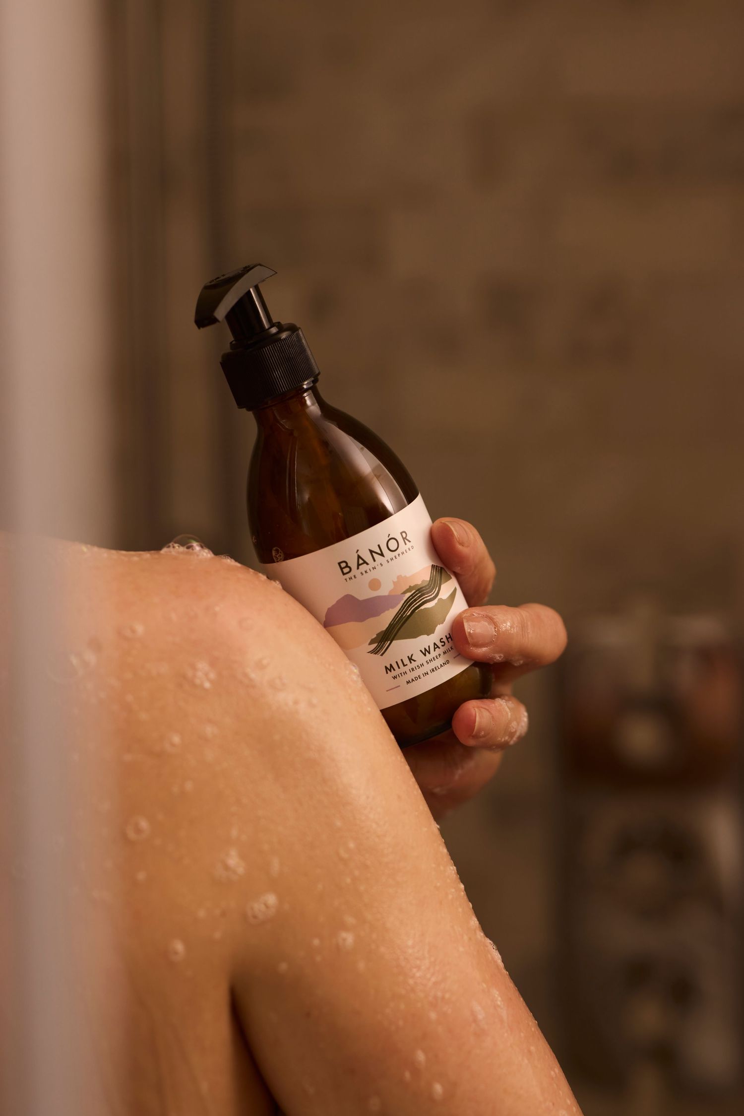 Person applying BANOR body scrub on their shoulder, showcasing the product's creamy texture against bare skin.