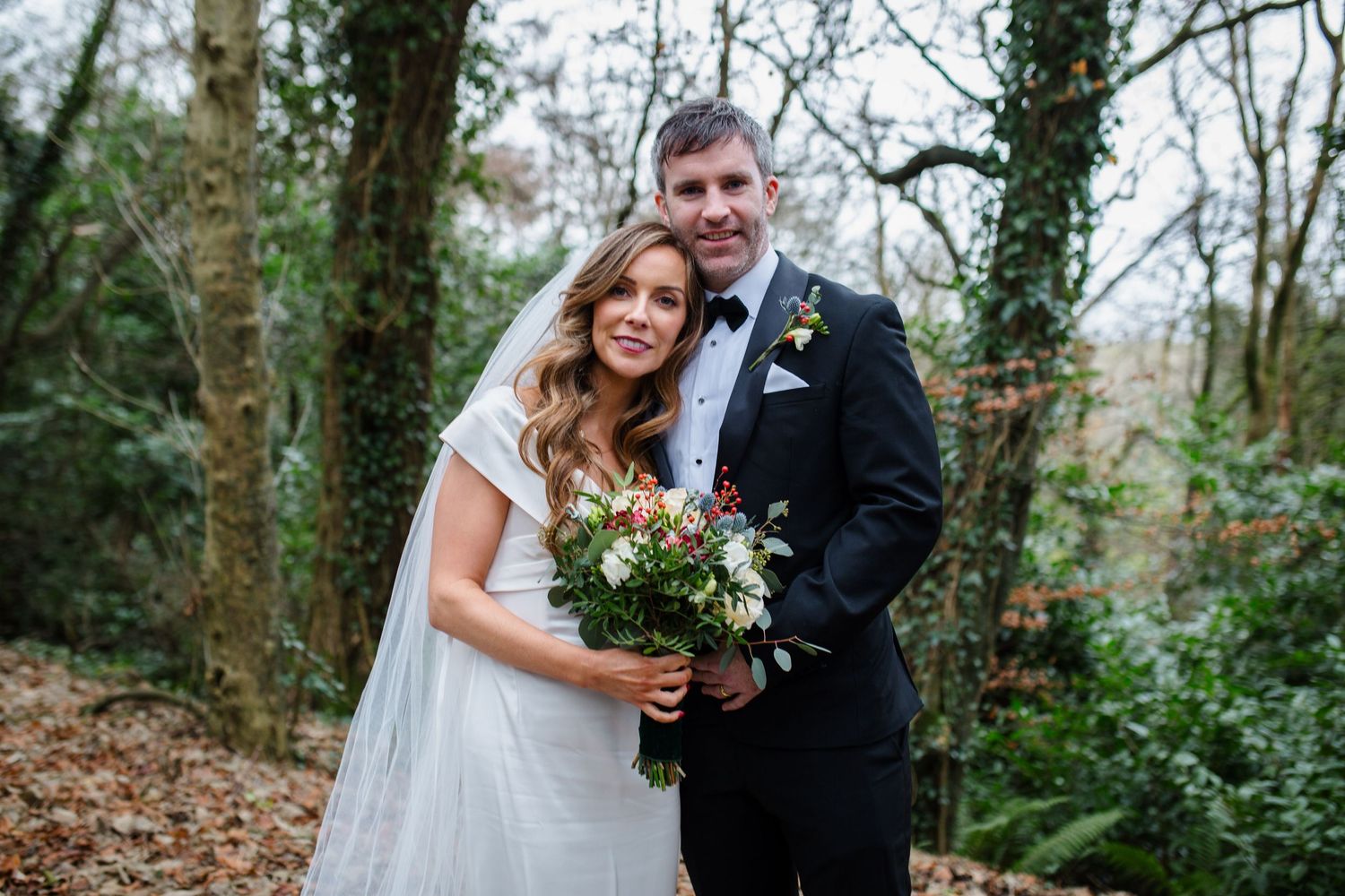 Bride and groom standing before a rustic white barn with red doors on their wedding day.