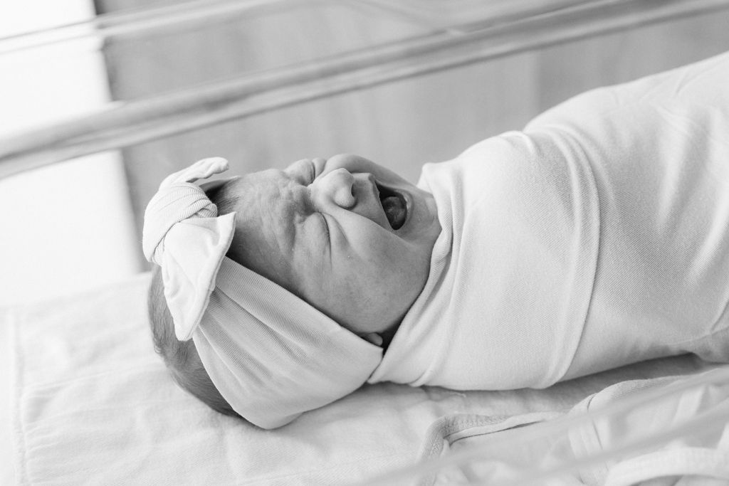 Black and white photo of a swaddled newborn baby crying in a hospital bassinet.