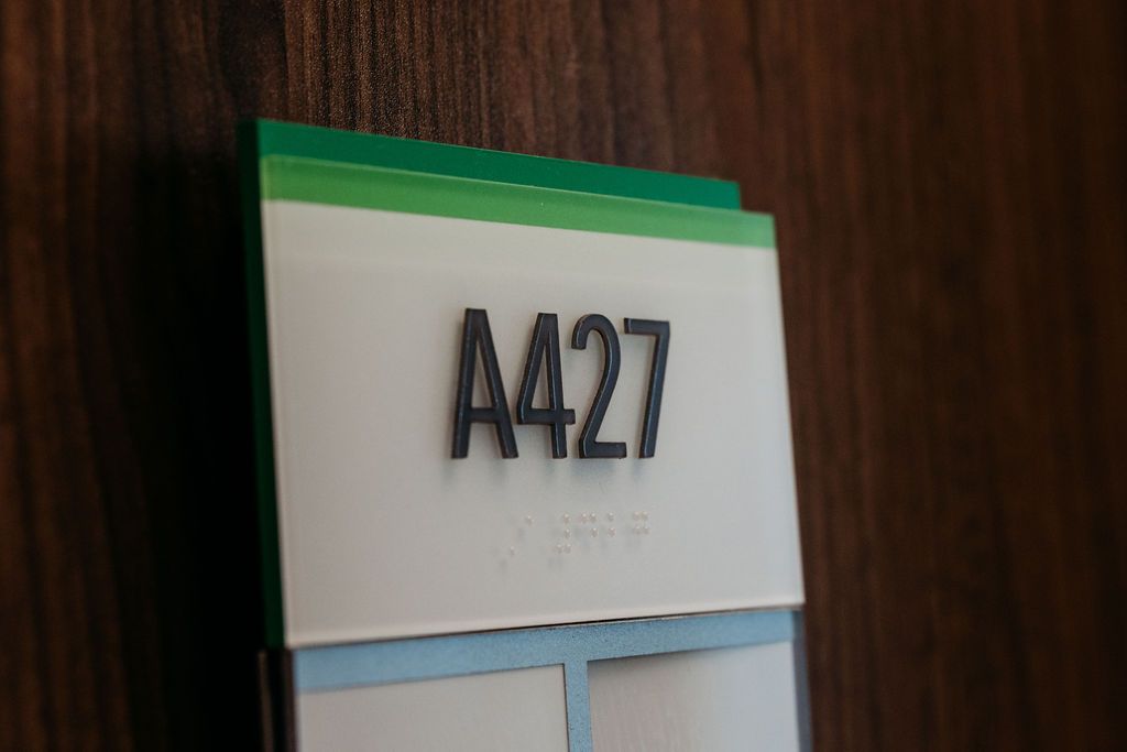 Close-up of room number sign A427 with Braille, featuring green and teal accents on a wood-paneled wall.