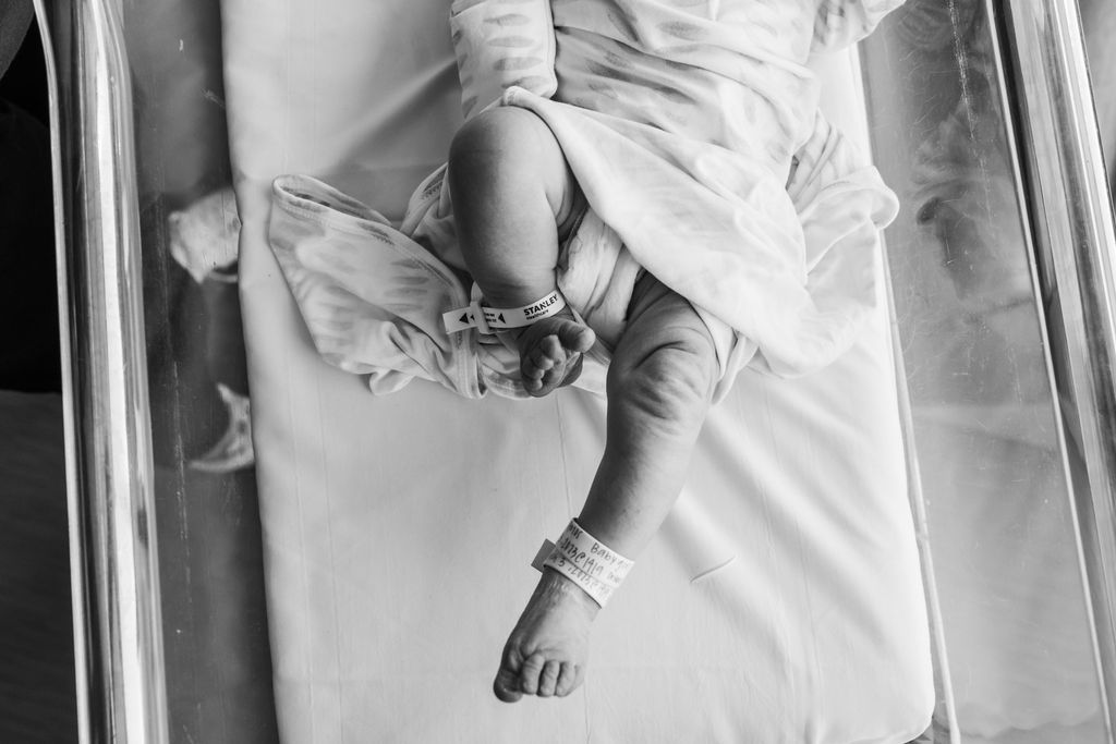 Black and white photo of a newborn baby lying in a hospital bassinet with identification bands on wrists and ankles.