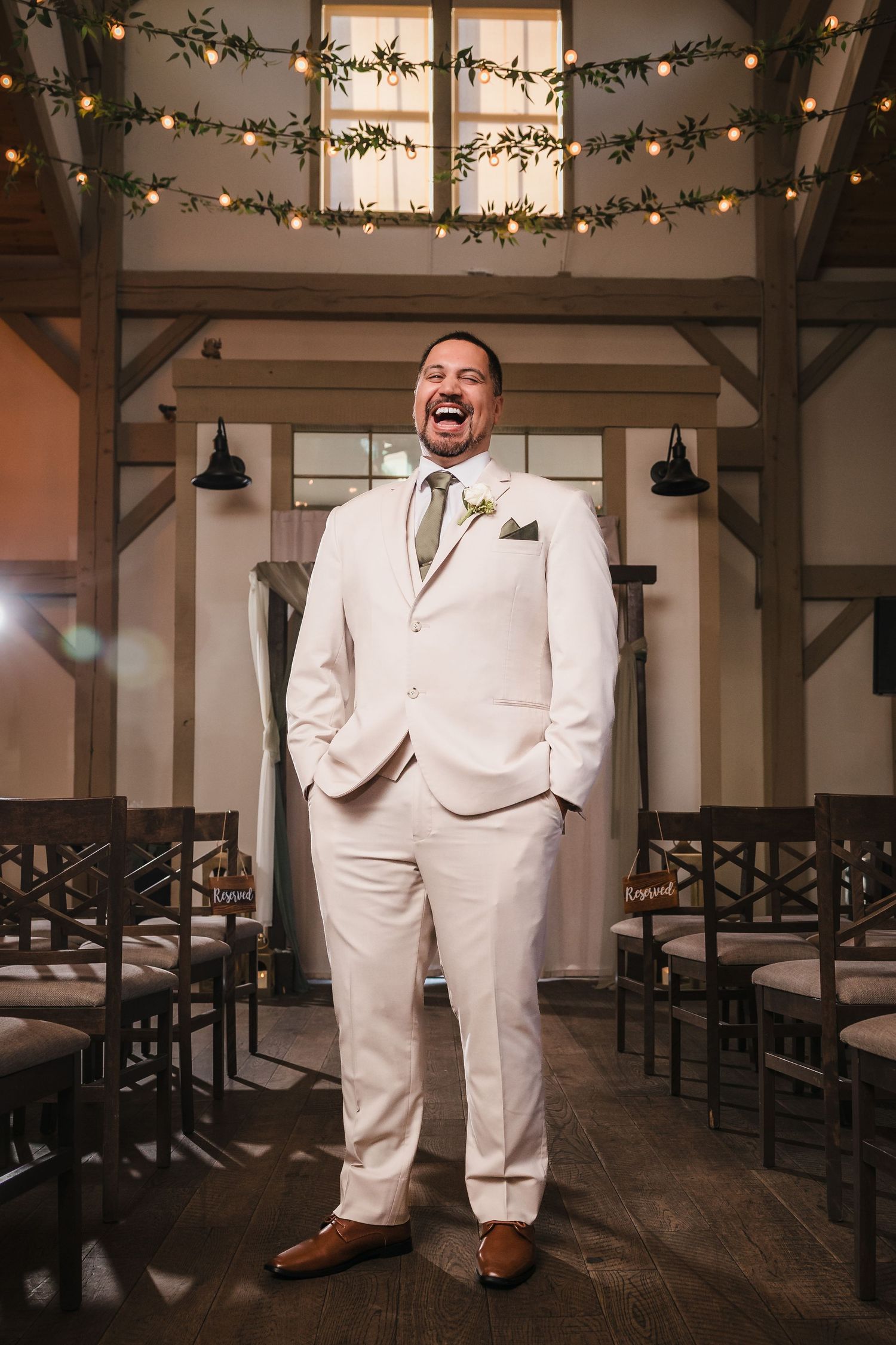 Groom laughing during solo portrait at Briar Barn Inn ceremony space with string lights and greenery overhead