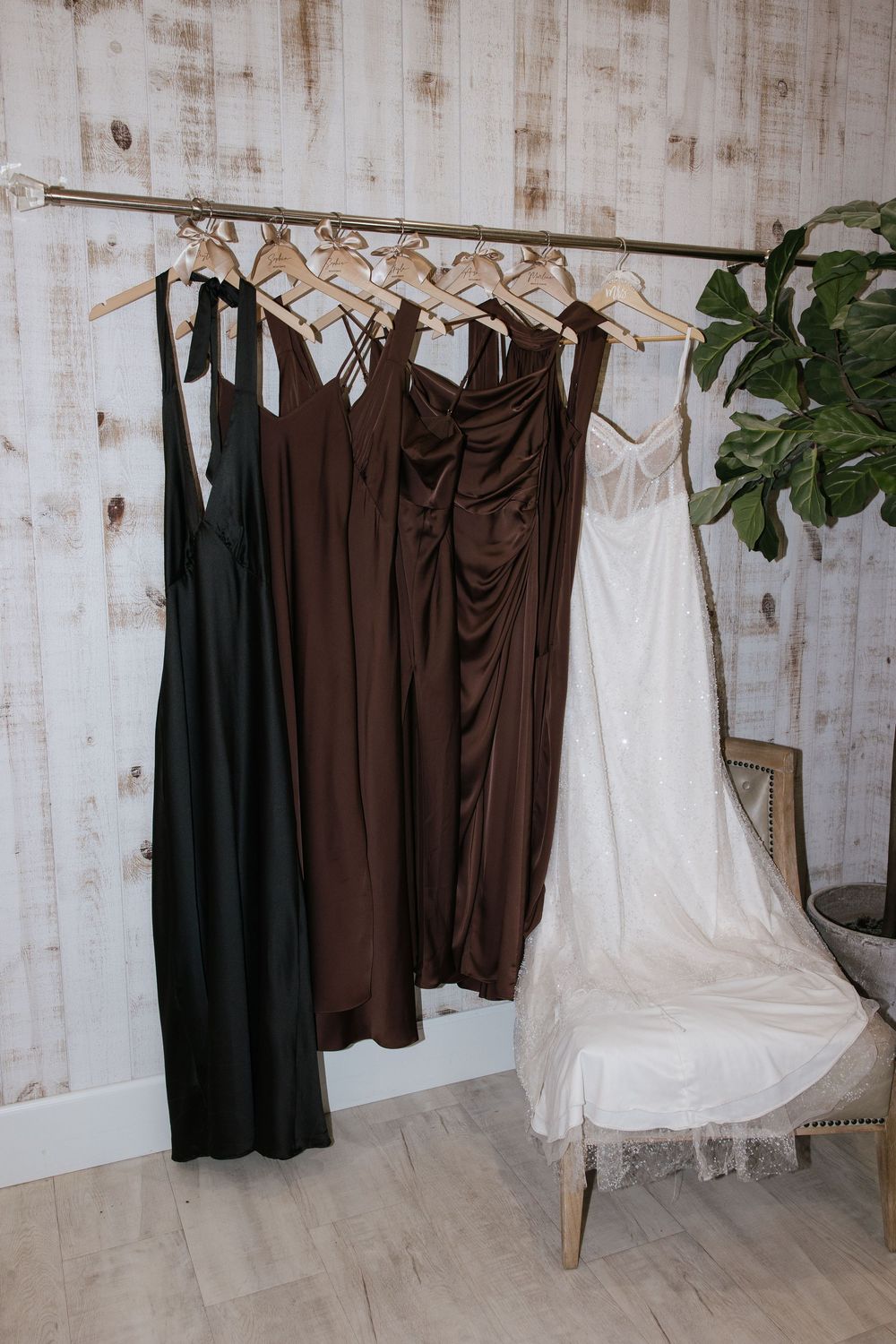 Brown satin bridesmaid dresses and white wedding gown hanging on a clothing rack.