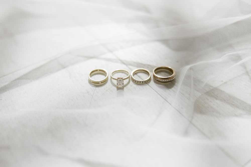 Three wedding rings arranged on white tulle fabric, featuring a diamond engagement ring flanked by two gold bands.