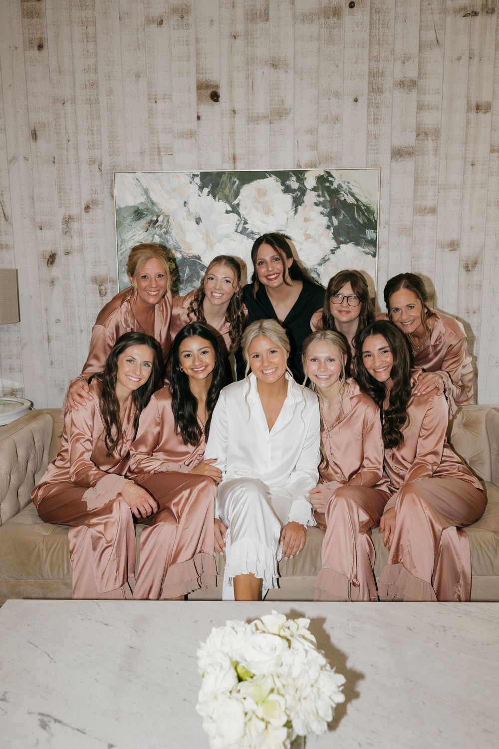 Bride poses with bridesmaids wearing dusty rose satin robes during wedding morning getting ready session.