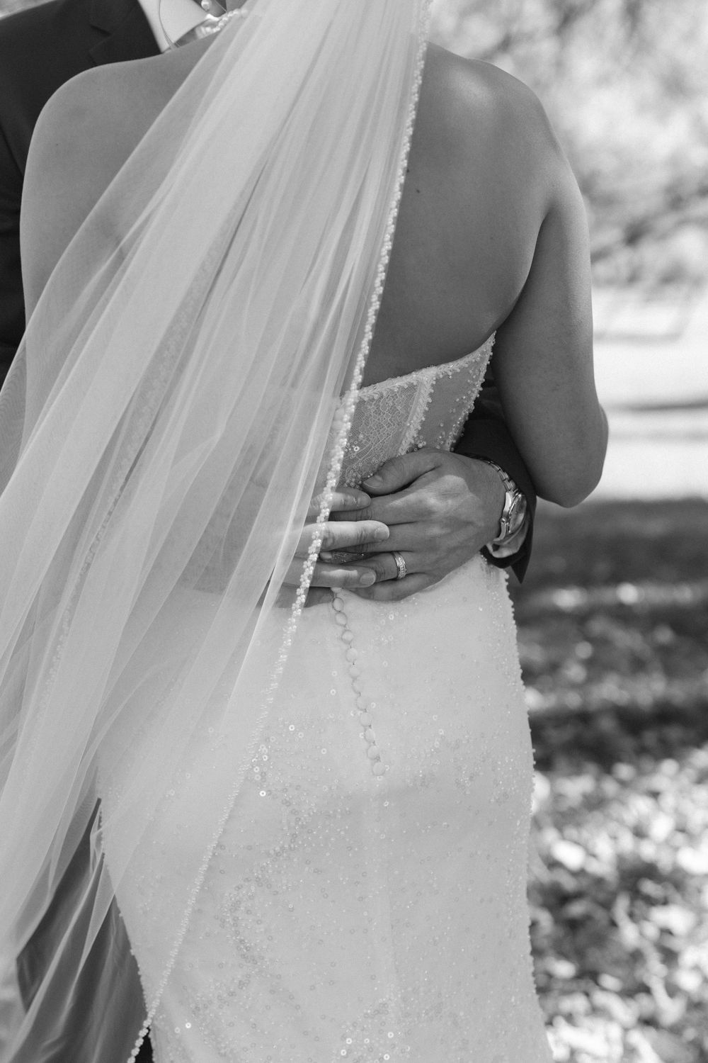 Black and white photo of groom's hand on bride's waist in lace wedding gown with veil.