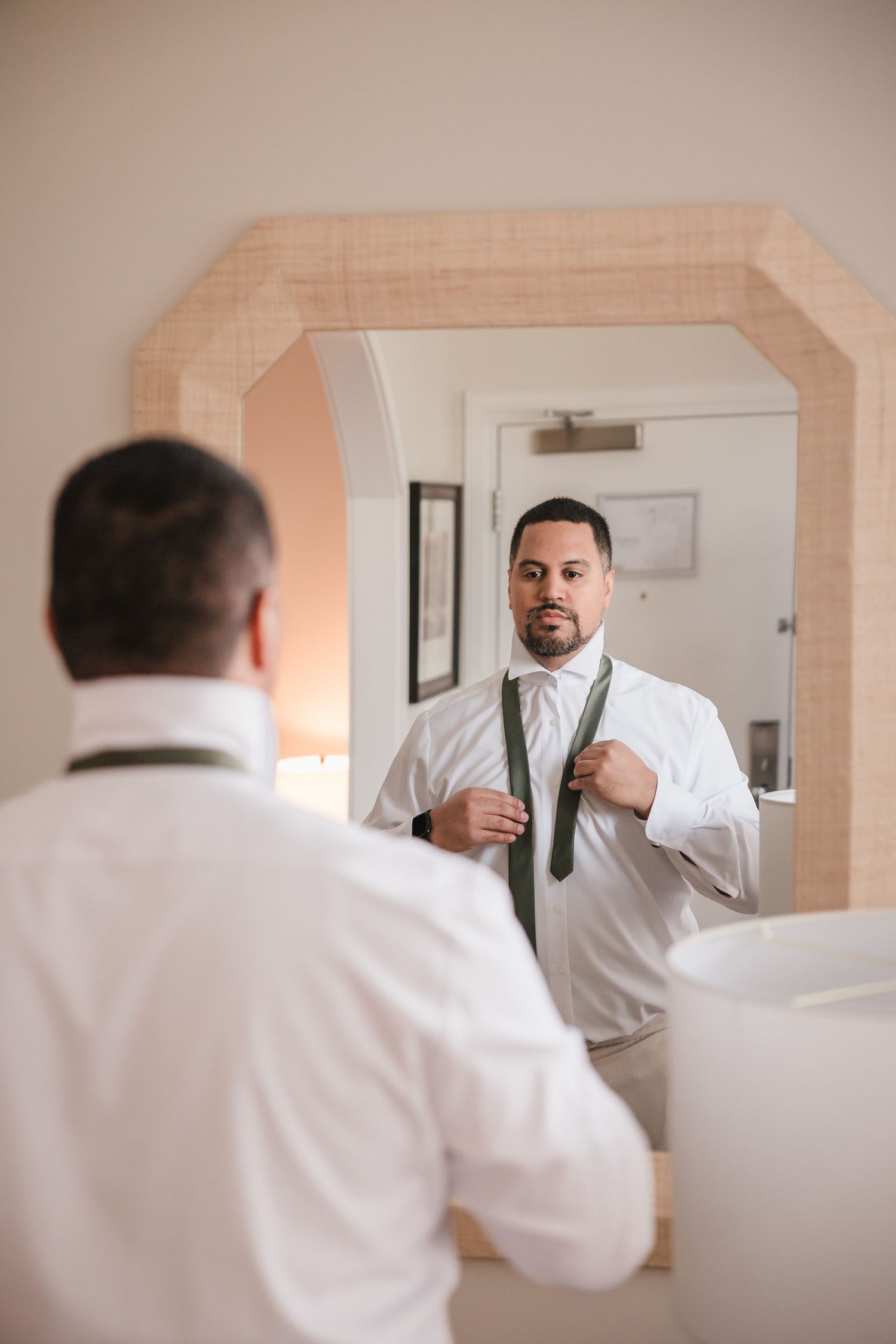 Groom adjusting tie in mirror during getting ready at Briar Barn Inn wedding Massachusetts