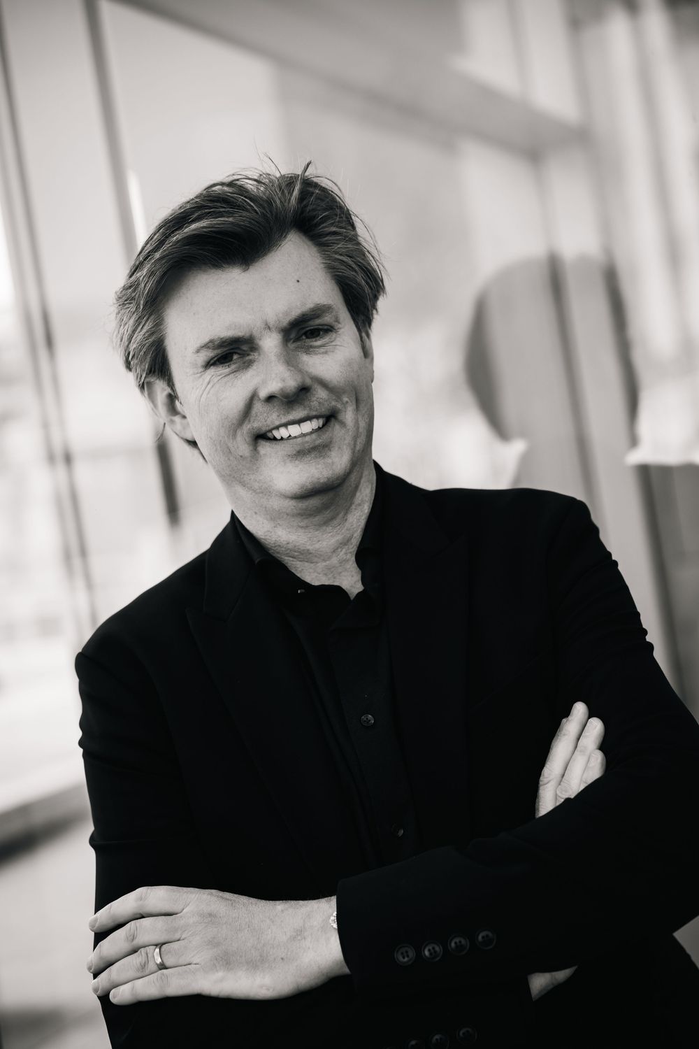 Smiling man in black jacket with arms crossed, black and white professional portrait photo.