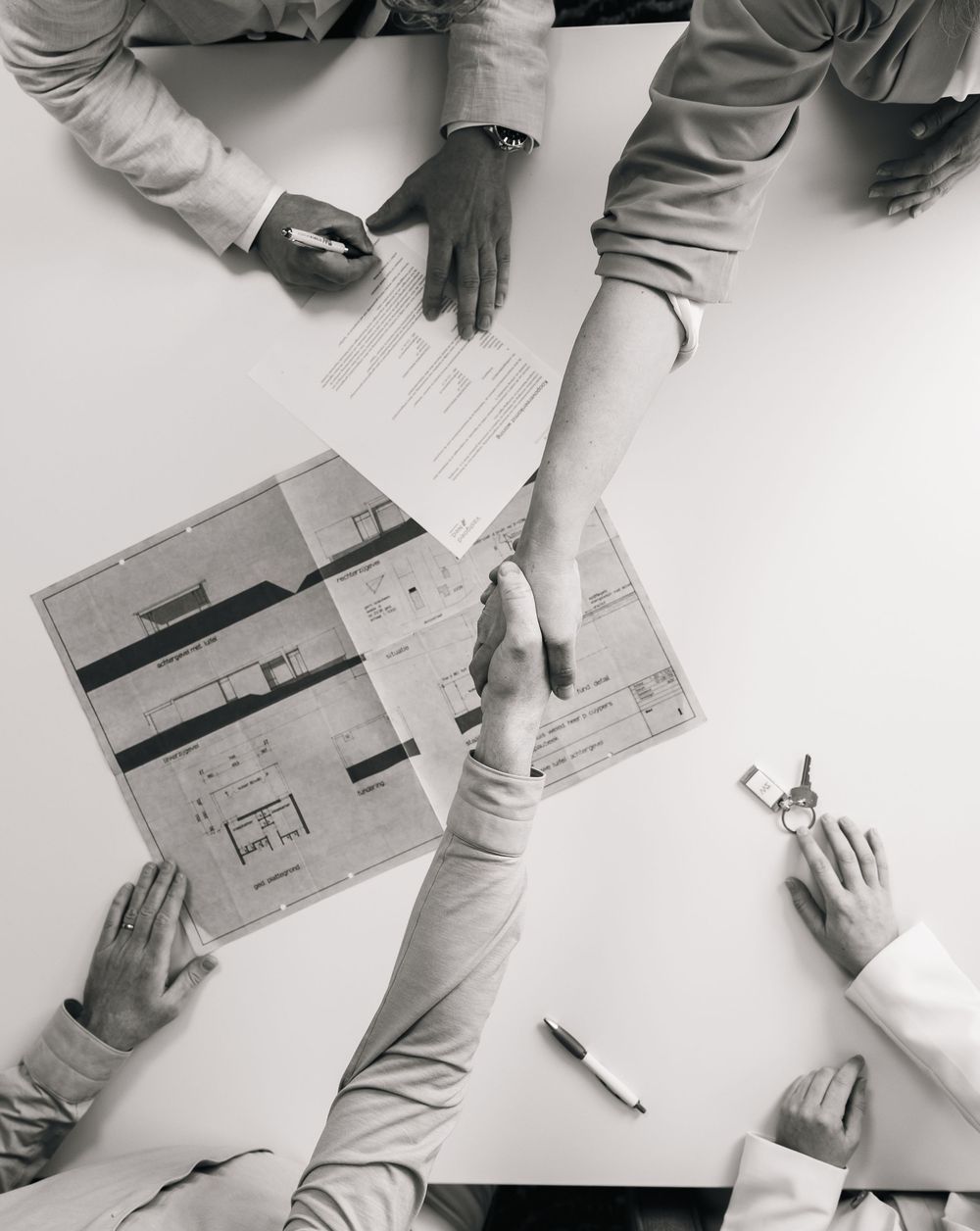 Aerial view of business people shaking hands over architectural blueprints at a meeting table.