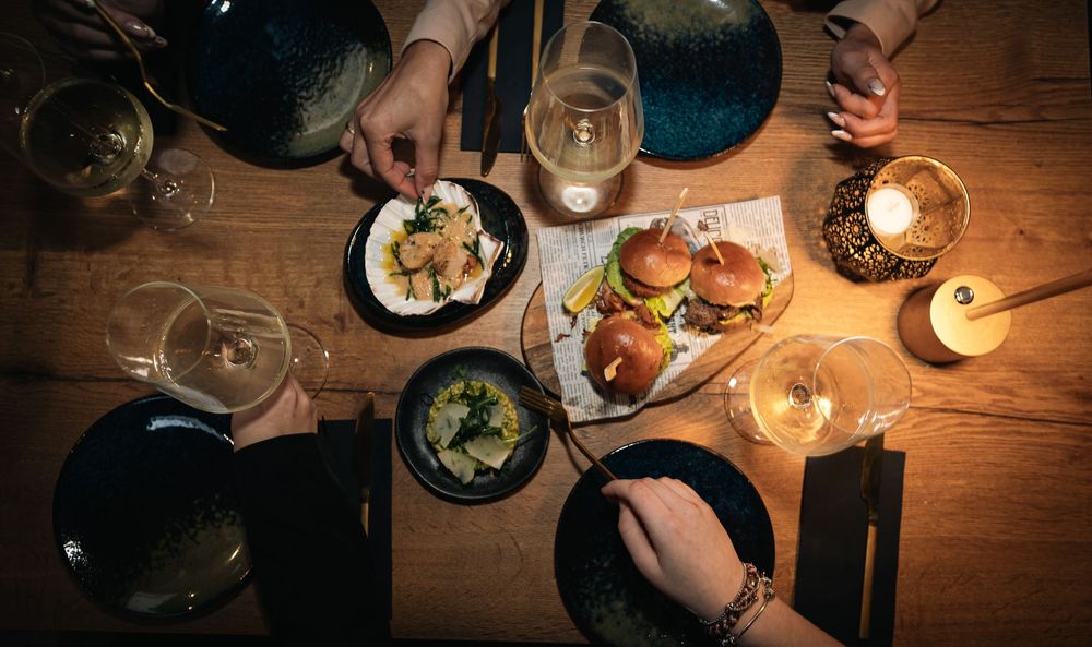 Overhead view of a candlelit dinner table with burgers, salads, and wine glasses shared between two people.