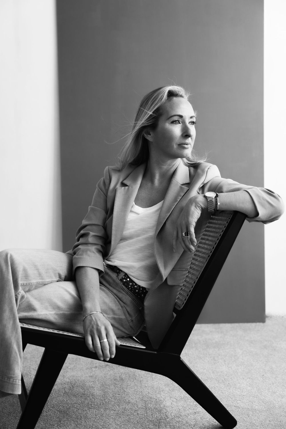 Black and white portrait of a blonde woman in blazer and jeans sitting relaxed in a modern chair.
