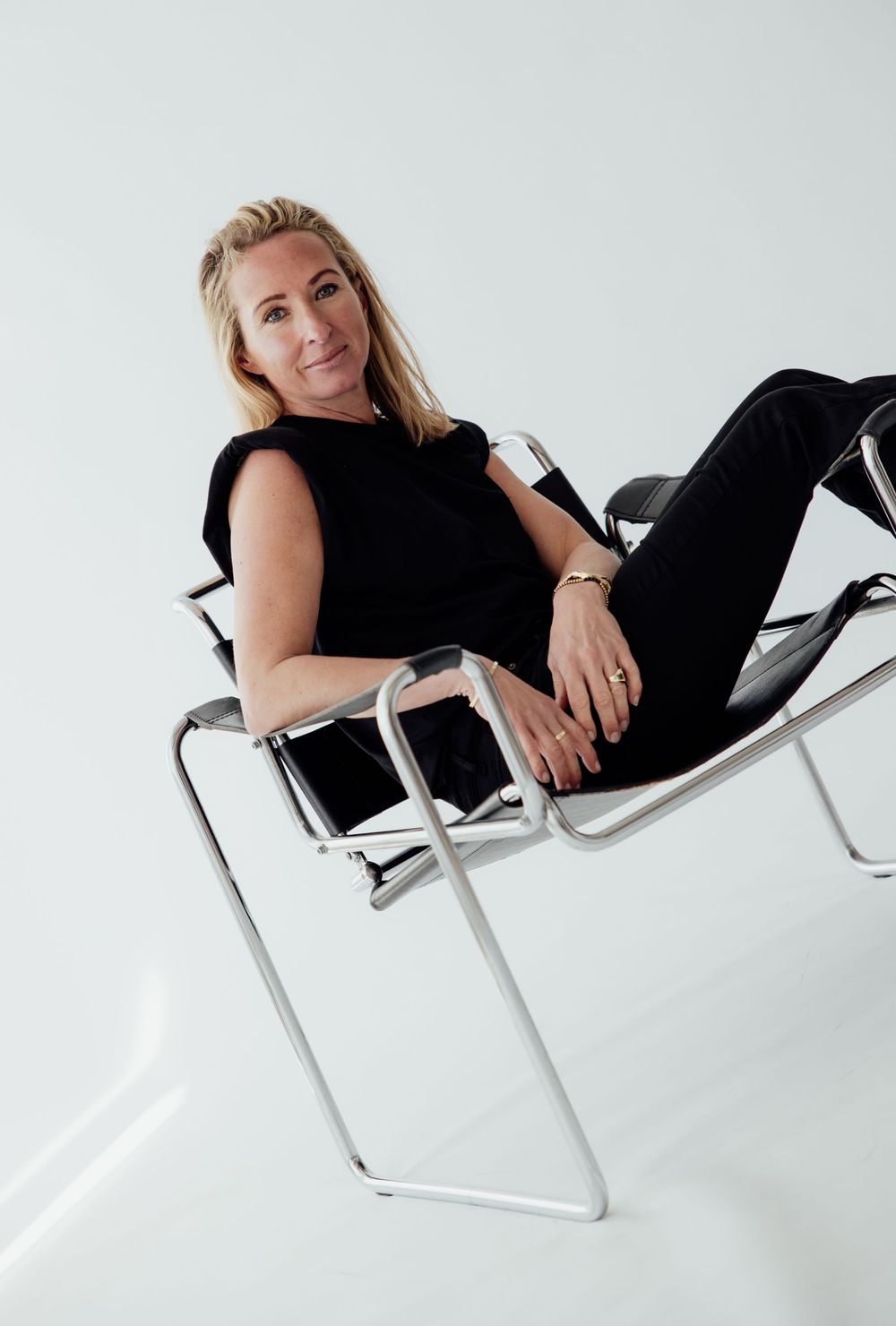 Woman in black outfit relaxing on a modern Wassily chair against a white background.