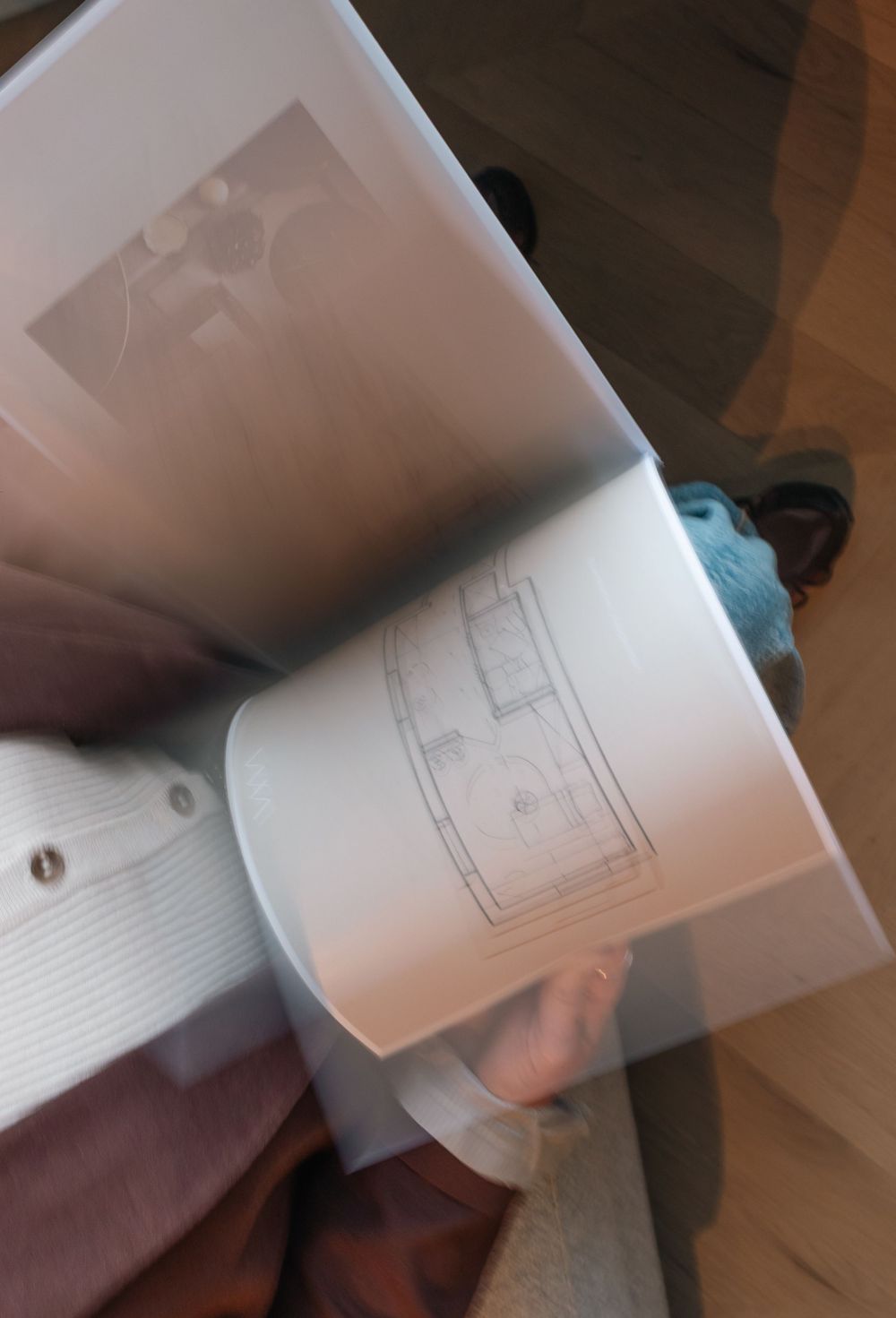 Person holding open a white binder with architectural floor plan sketches and a photo inside.