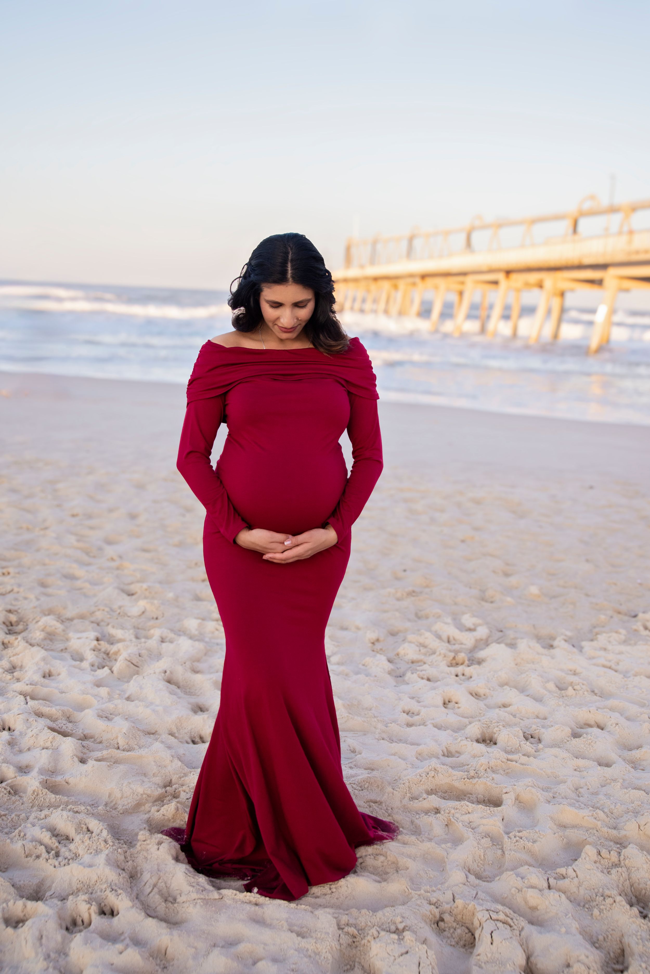 mother in a red maternity gown supplied by the photographer on the beach