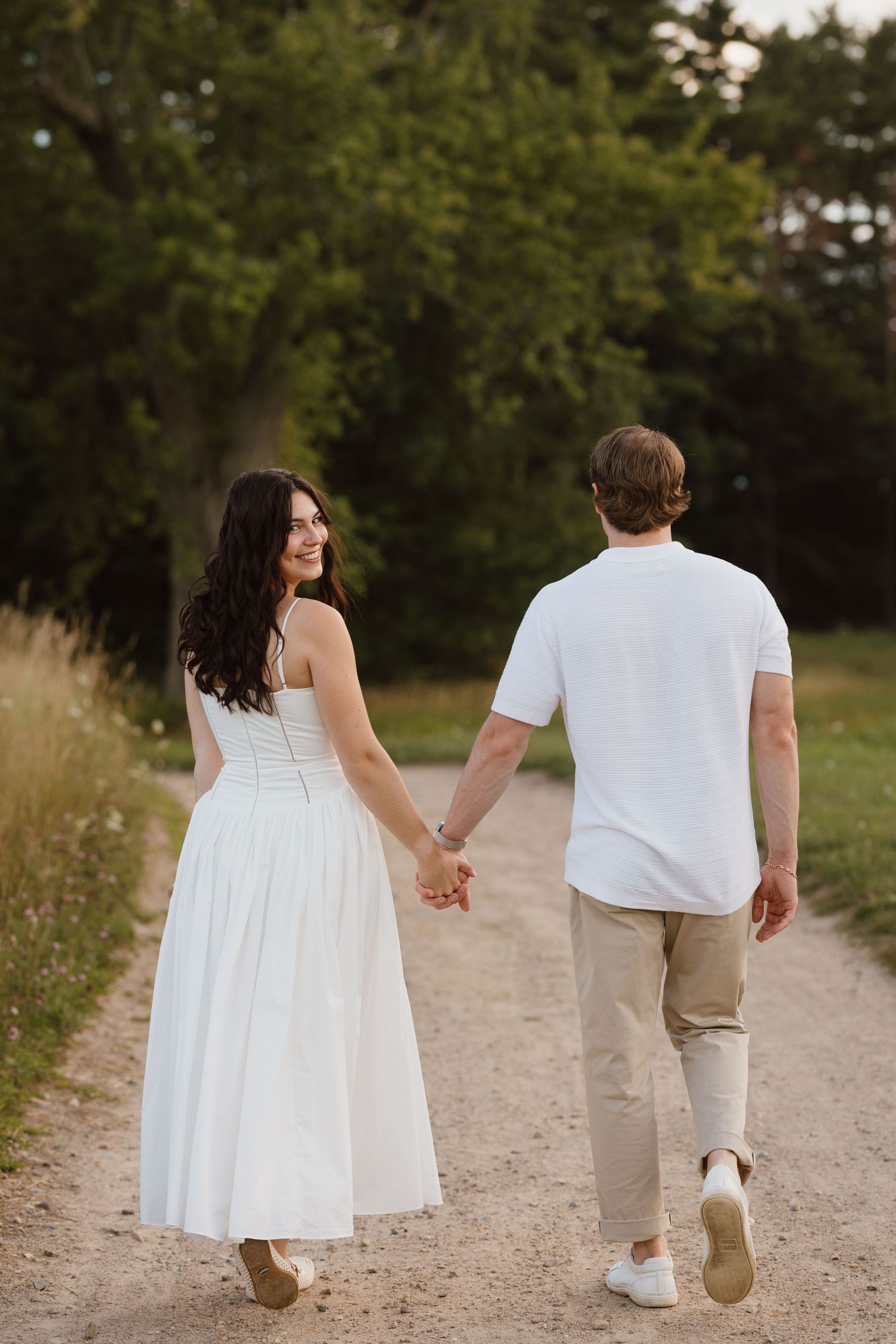 A couple shares a romantic kiss on sandy beach dunes at sunset, woman in white dress, man in white shirt.