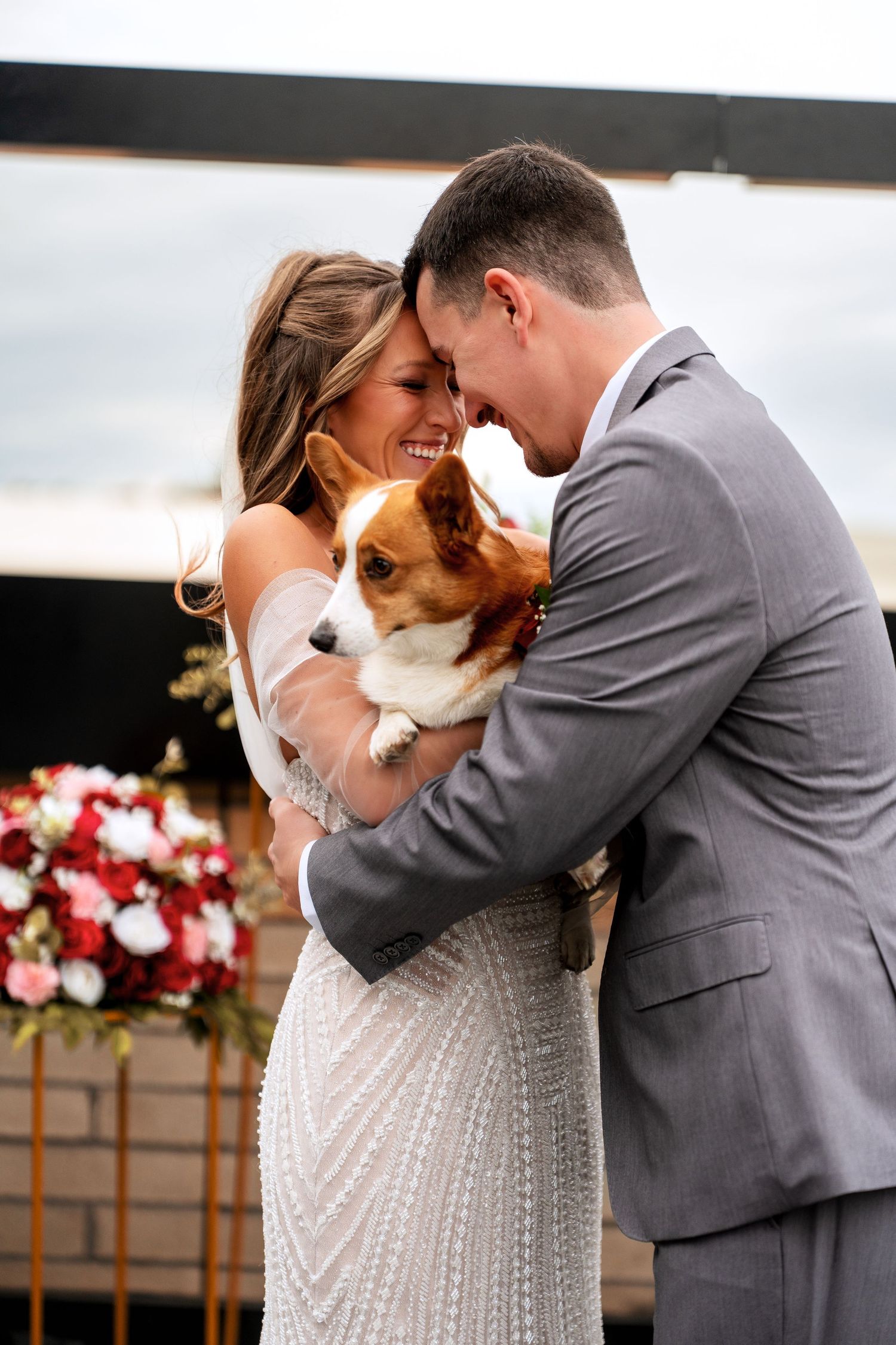 Bride and groom touch foreheads while holding an adorable corgi dog at their wedding ceremony.