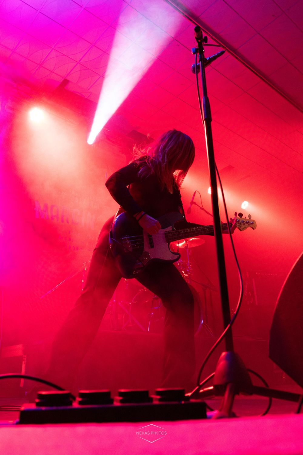 Guitarist performing on stage bathed in vibrant pink and red lighting with dramatic fog effects during a live concert.
