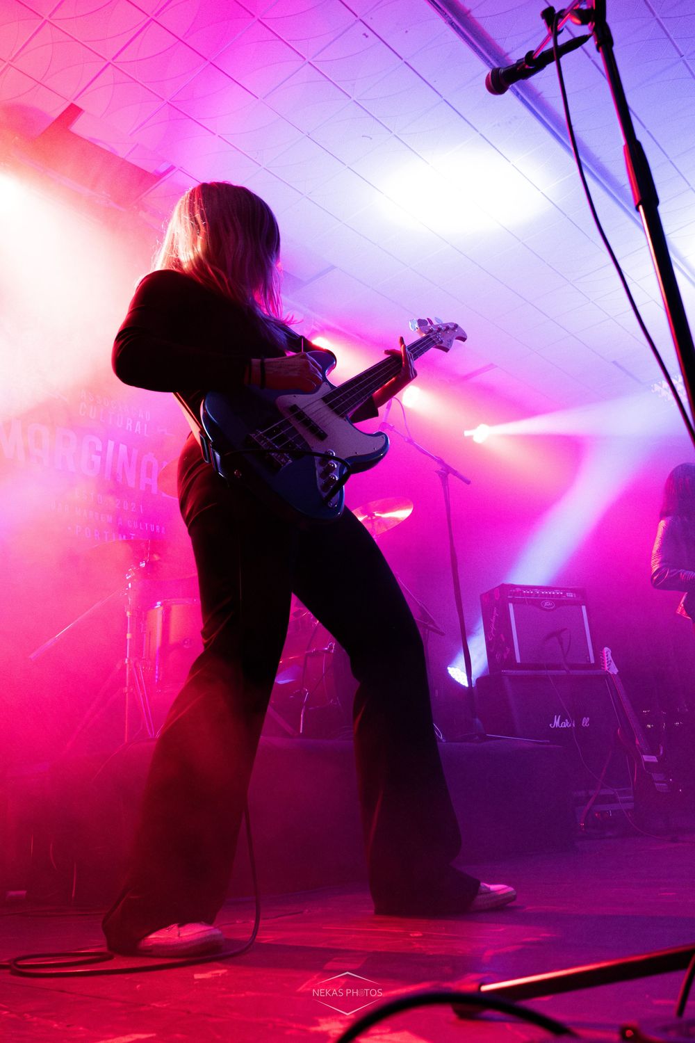 Female guitarist performing on stage bathed in vibrant pink and purple lights during a live rock concert.