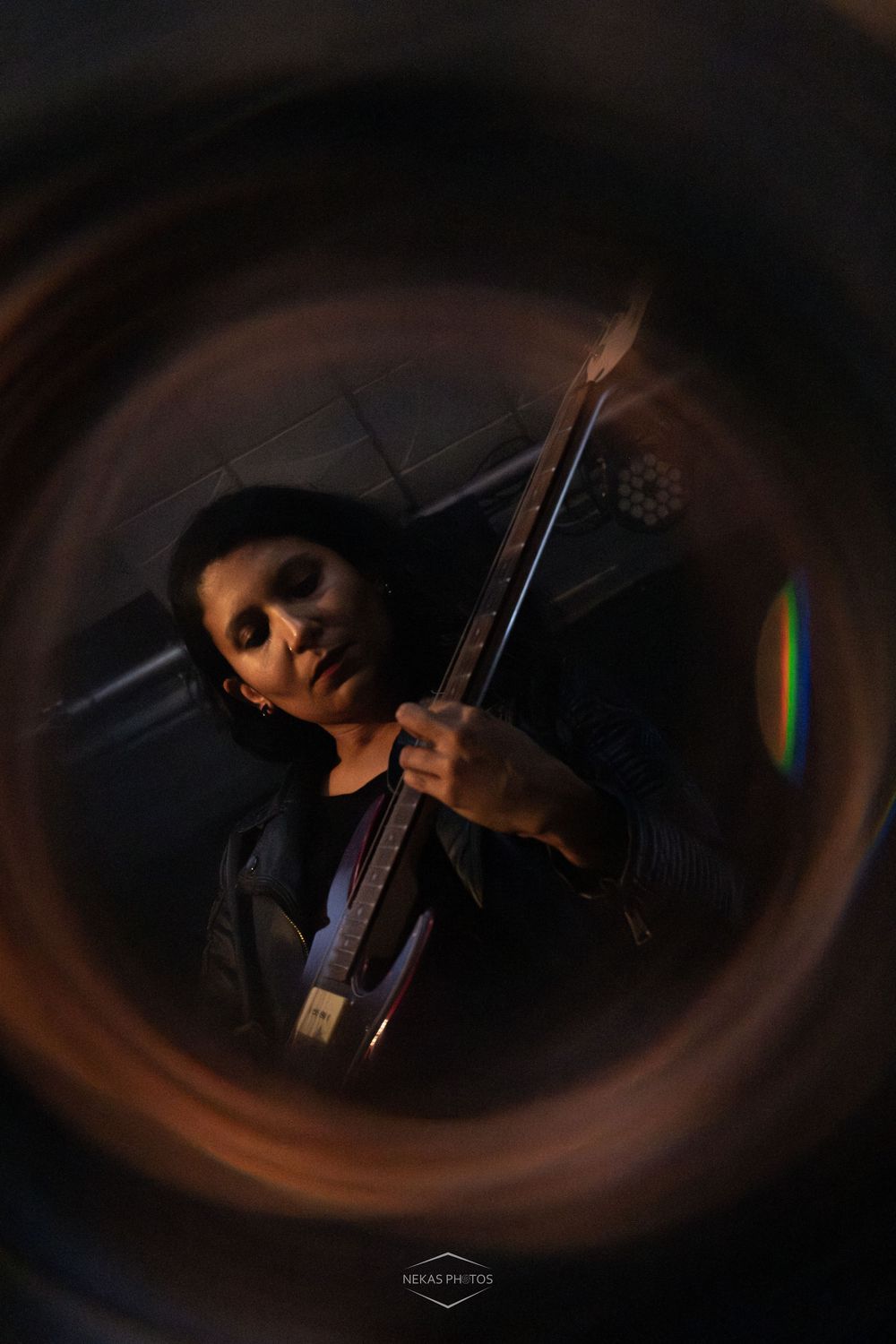Musician playing electric guitar captured through a circular lens vignette in dramatic dark moody lighting.