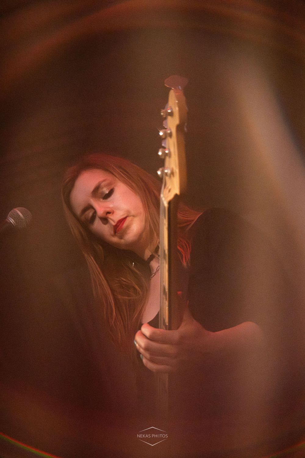 Young woman with red hair plays guitar on stage under warm amber stage lighting.