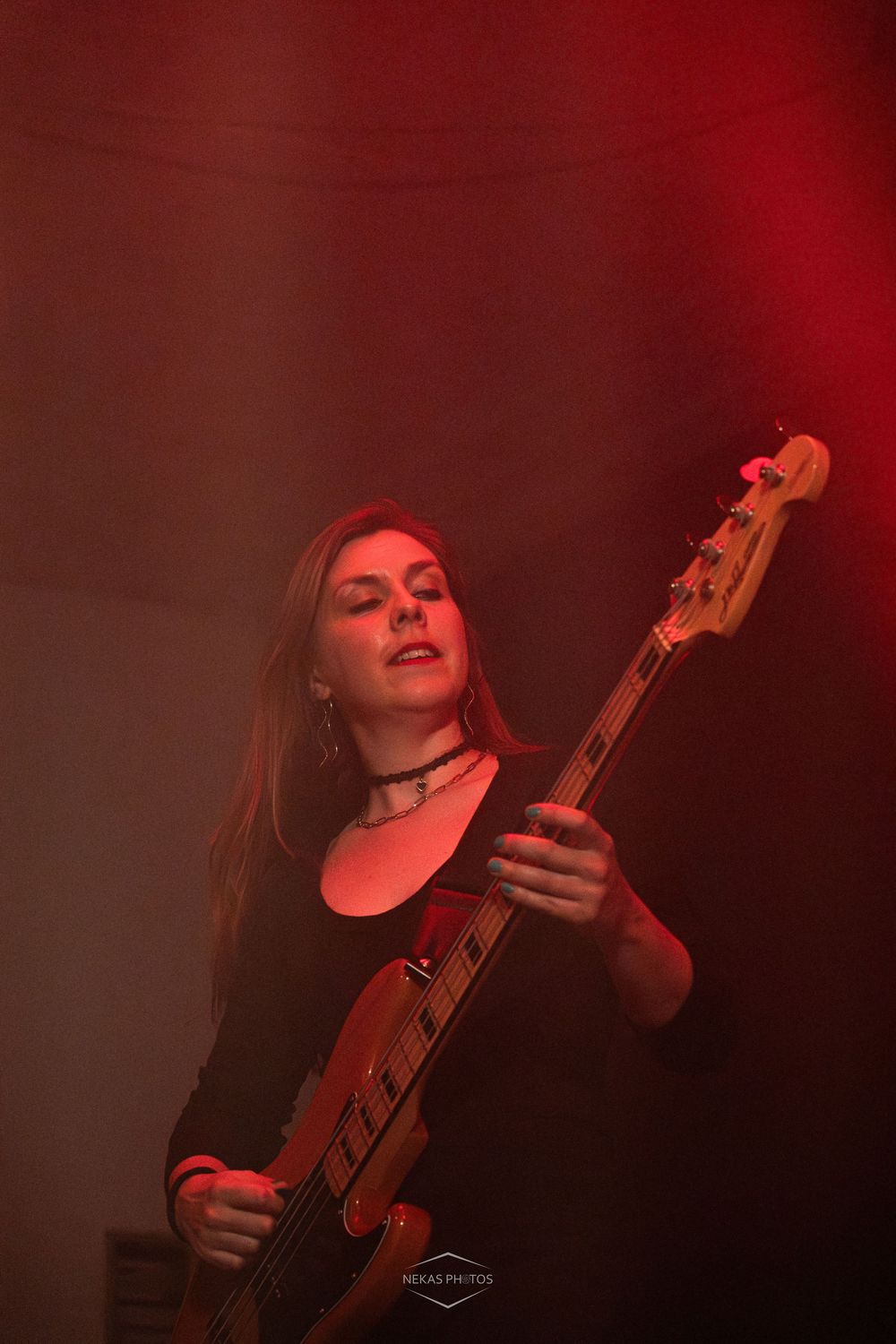 Young woman playing bass guitar on stage under dramatic red lighting at a live music concert.