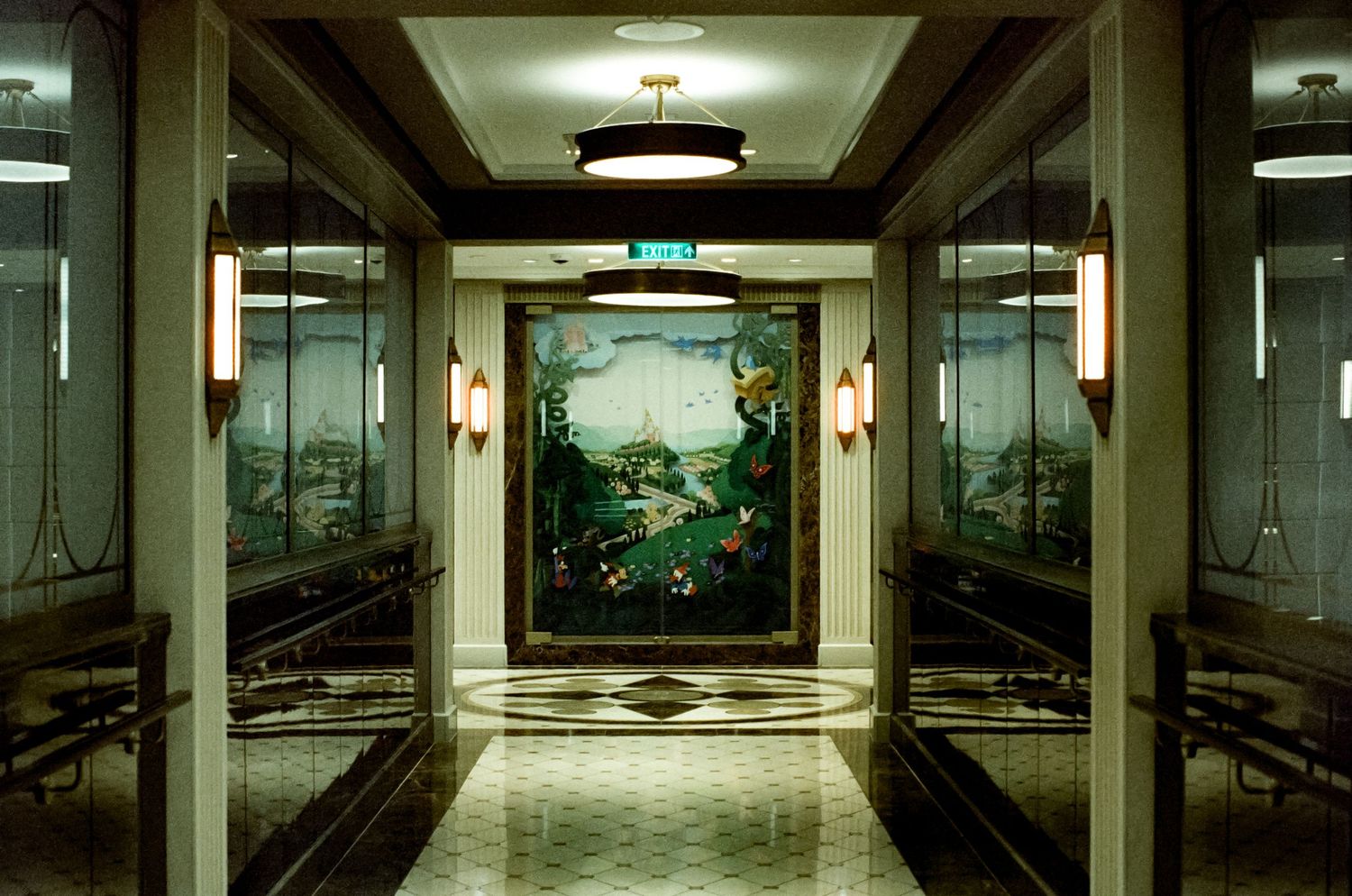 Elegant hotel corridor with ornate landscape mural, mirrored walls, brass sconces, and checkered marble floor.