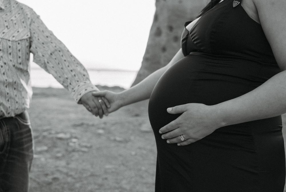 Black and white photo of a pregnant couple holding hands outdoors, showcasing baby bump.