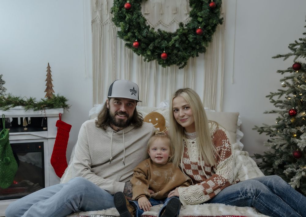 Family of three posing for a Christmas photo with festive decorations and tree. Bismarck, ND photographer
