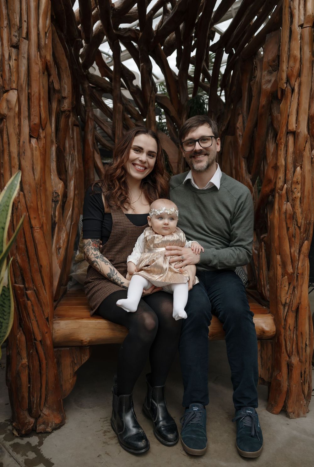 Happy family with tattooed mother, bearded father, and baby girl sitting on a rustic wooden bench outdoors. Bismarck, ND photographer