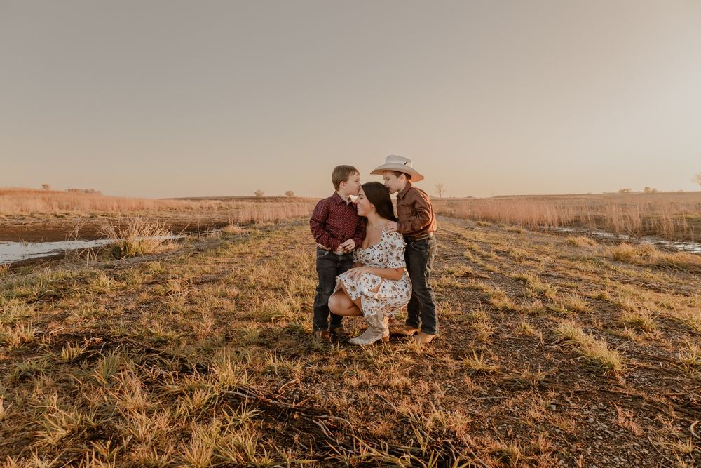 Family of three sharing a tender moment in a golden field at sunset, with parents embracing their young son. Garrison, ND Photographer