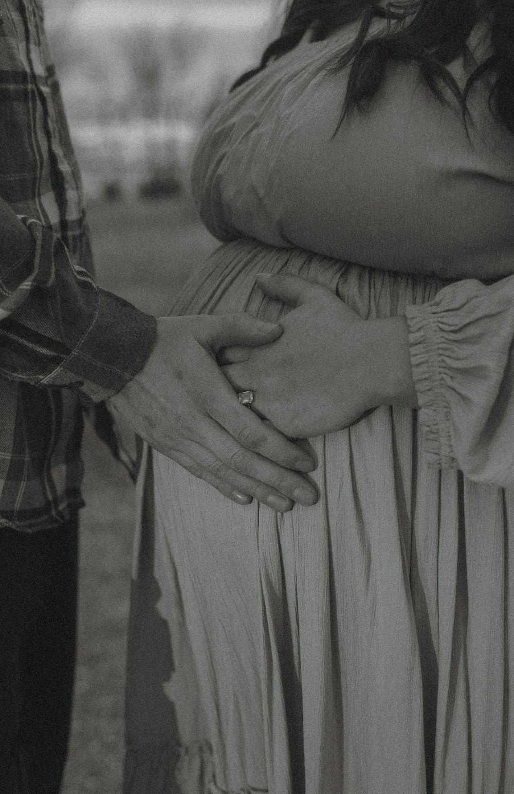 Black and white maternity photo of a couple, man placing hand on pregnant woman's belly, wearing a diamond ring. Garrison, ND Photographer