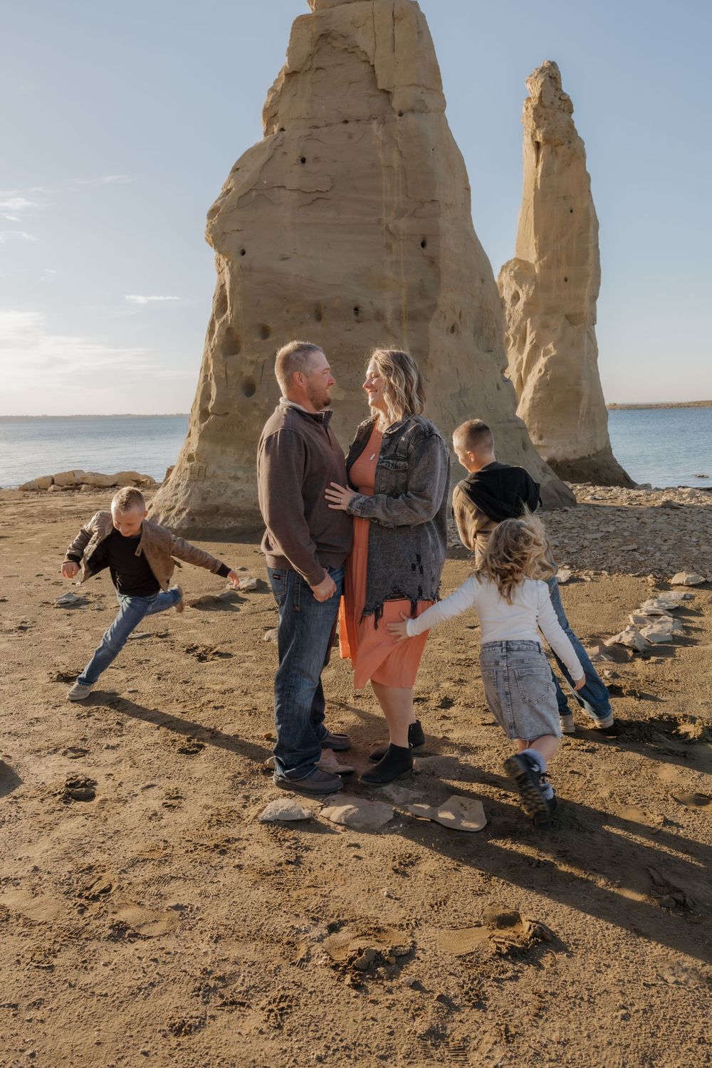 Family of five enjoying a sunny day on a sandy beach with tall rock spires. Garrison, ND Photographer