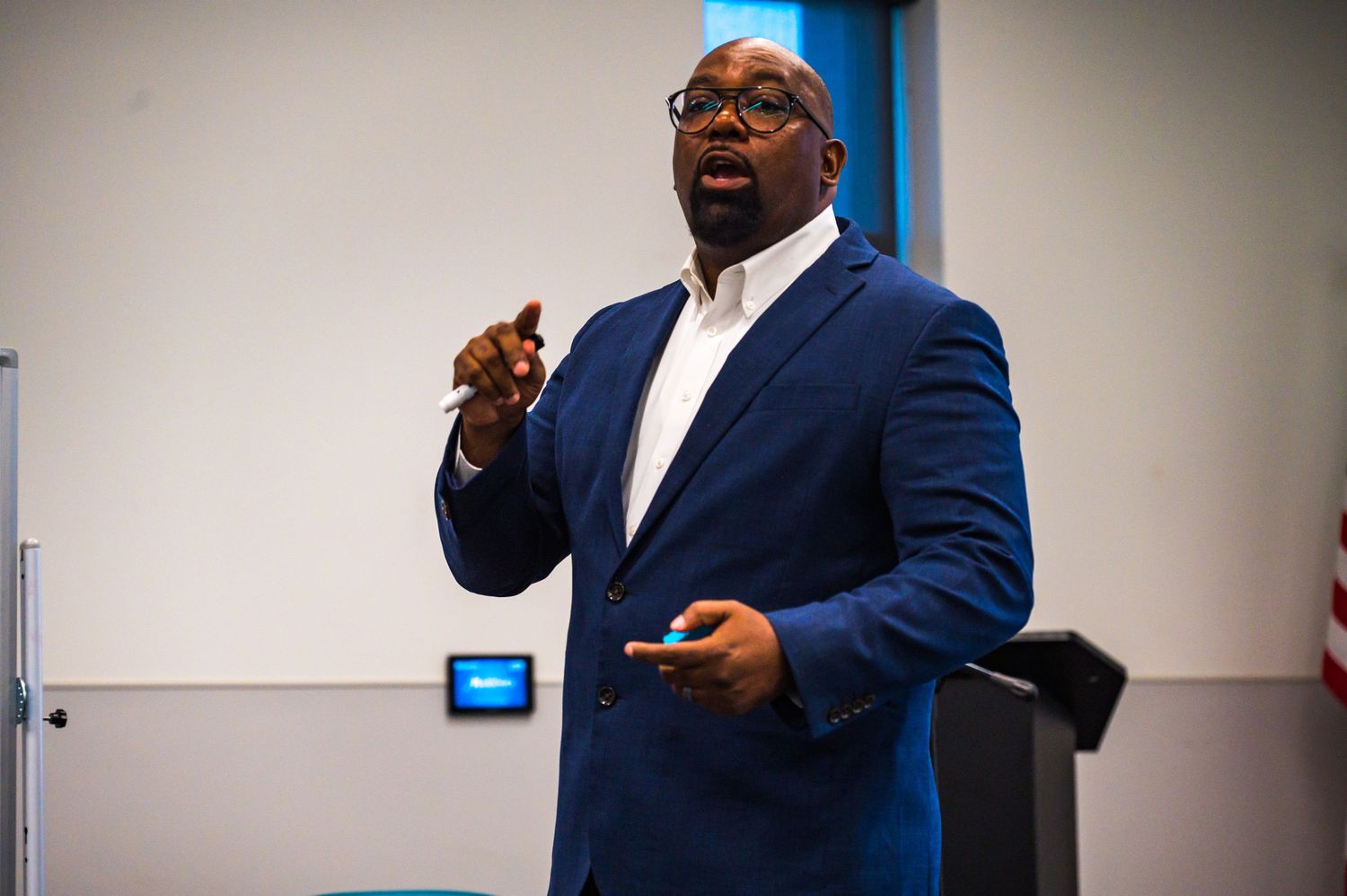 Confident male speaker in blue blazer gesturing during a professional presentation indoors.