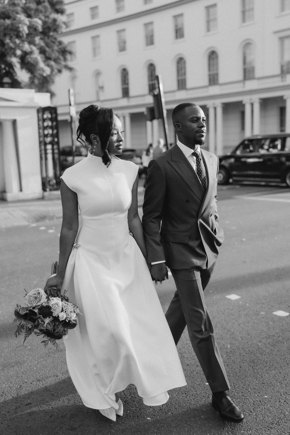 Black and white photo of a bride and groom holding hands while crossing a city street on their wedding day.