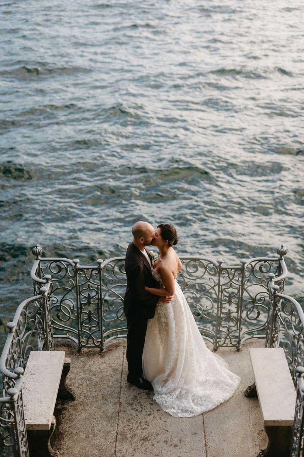 Bride and groom share a romantic kiss on an ornate balcony overlooking the ocean on their wedding day in Lake Como.