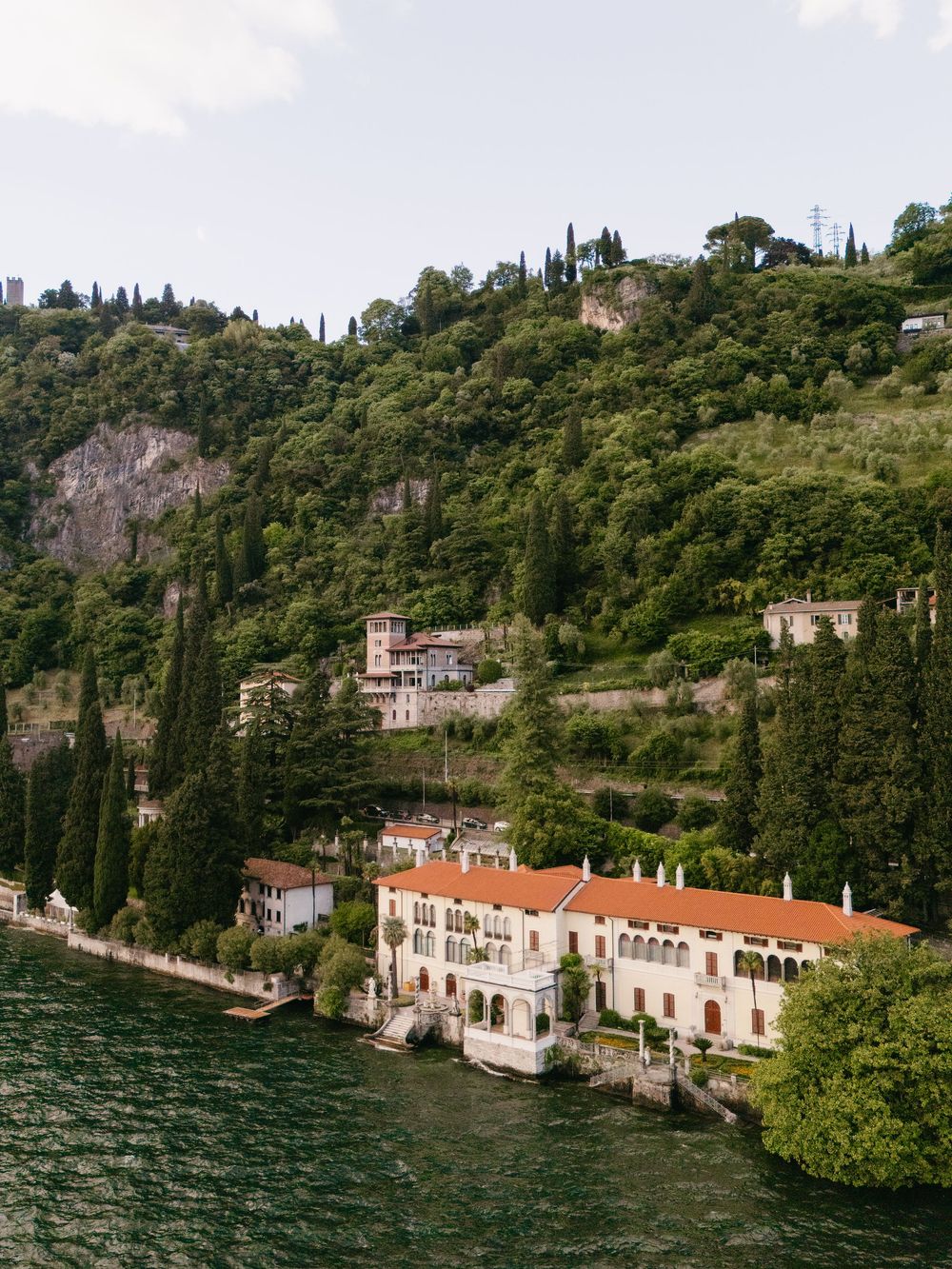 Aerial view of a grand Italian villa with red roof nestled on the lush shores of Lake Como.