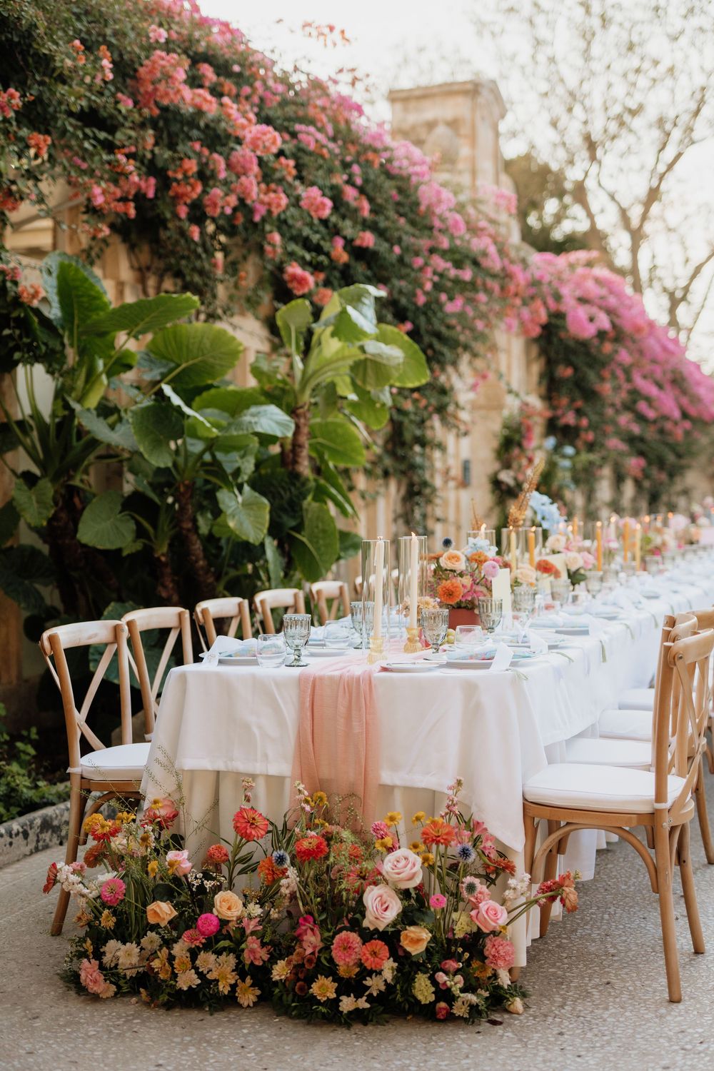 Elegant outdoor wedding reception table with pink floral arrangements, candles, and bougainvillea backdrop.