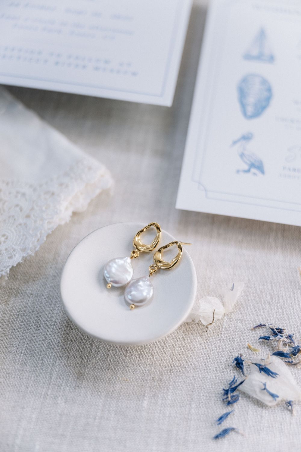 Gold hoop earrings with baroque pearl drops displayed on white ceramic dish with blue floral stationery.