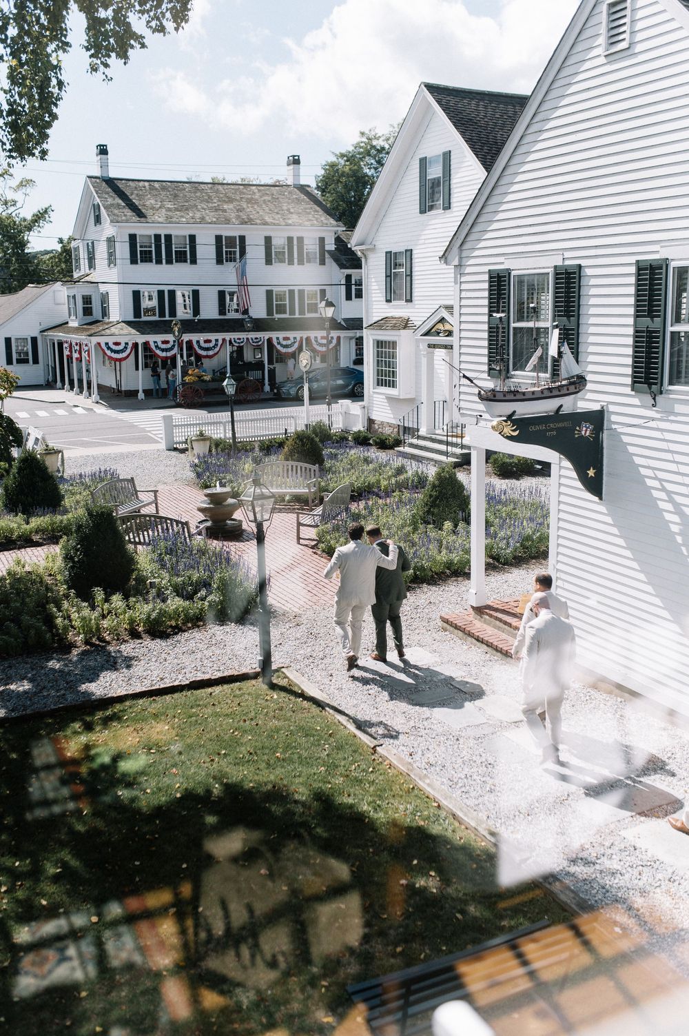 Aerial view of wedding guests arriving at a charming white New England inn with manicured gardens.