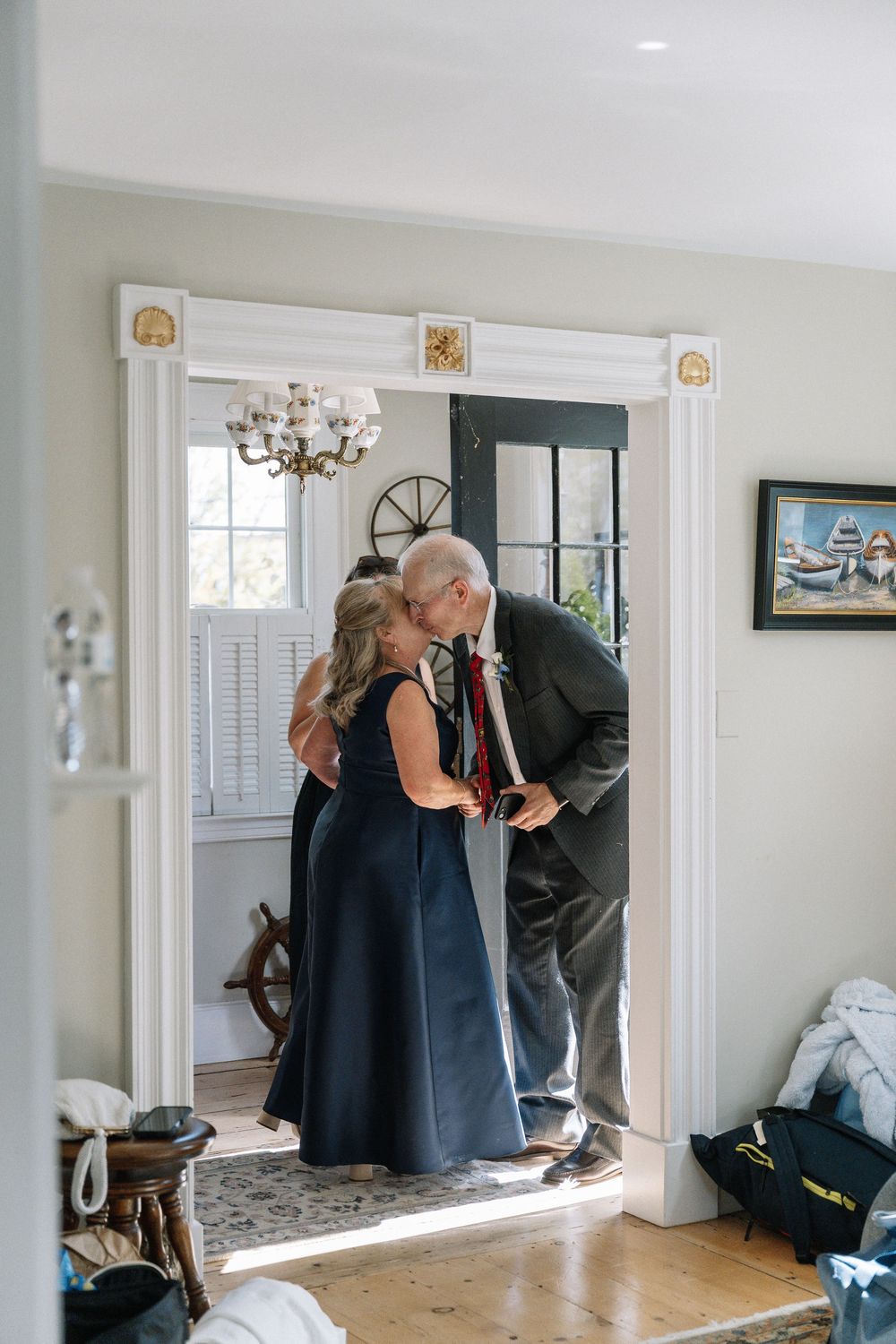 Older couple sharing a tender kiss in a sunlit doorway during wedding day preparations.