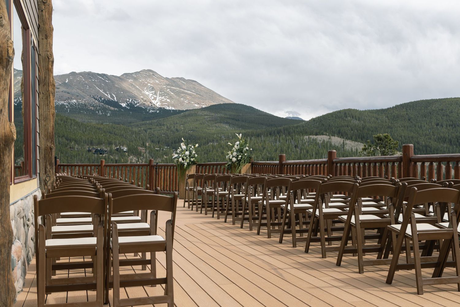 Outdoor wedding ceremony setup on a mountain deck with wooden chairs, floral arrangements, and stunning Rocky Mountain views.