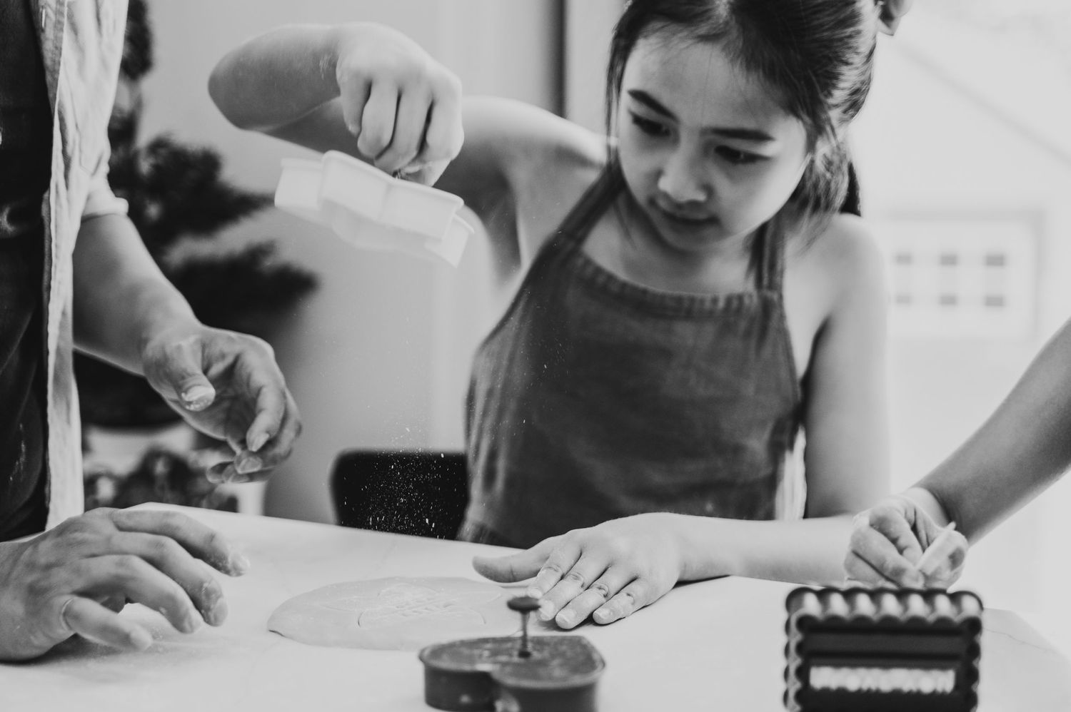 A little girl concentrates and lifts a cookie cutter from the dough and flour falls from it