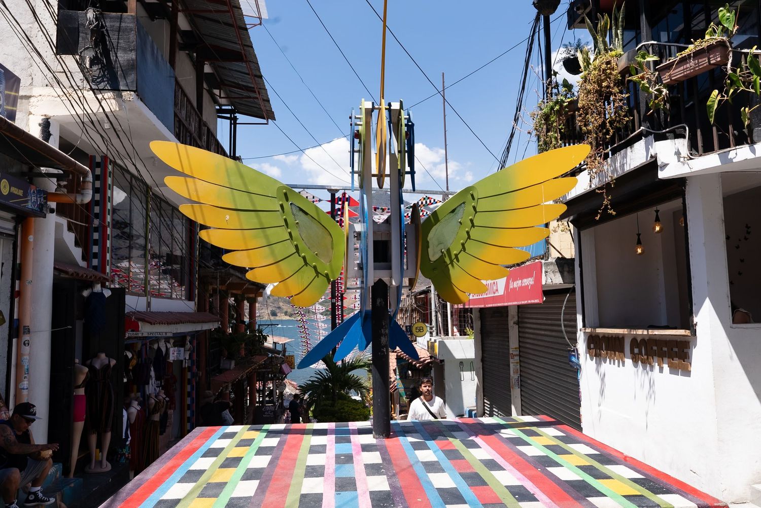Colorful banners and flags hang over a narrow street in a Latin American town, creating a festive atmosphere.