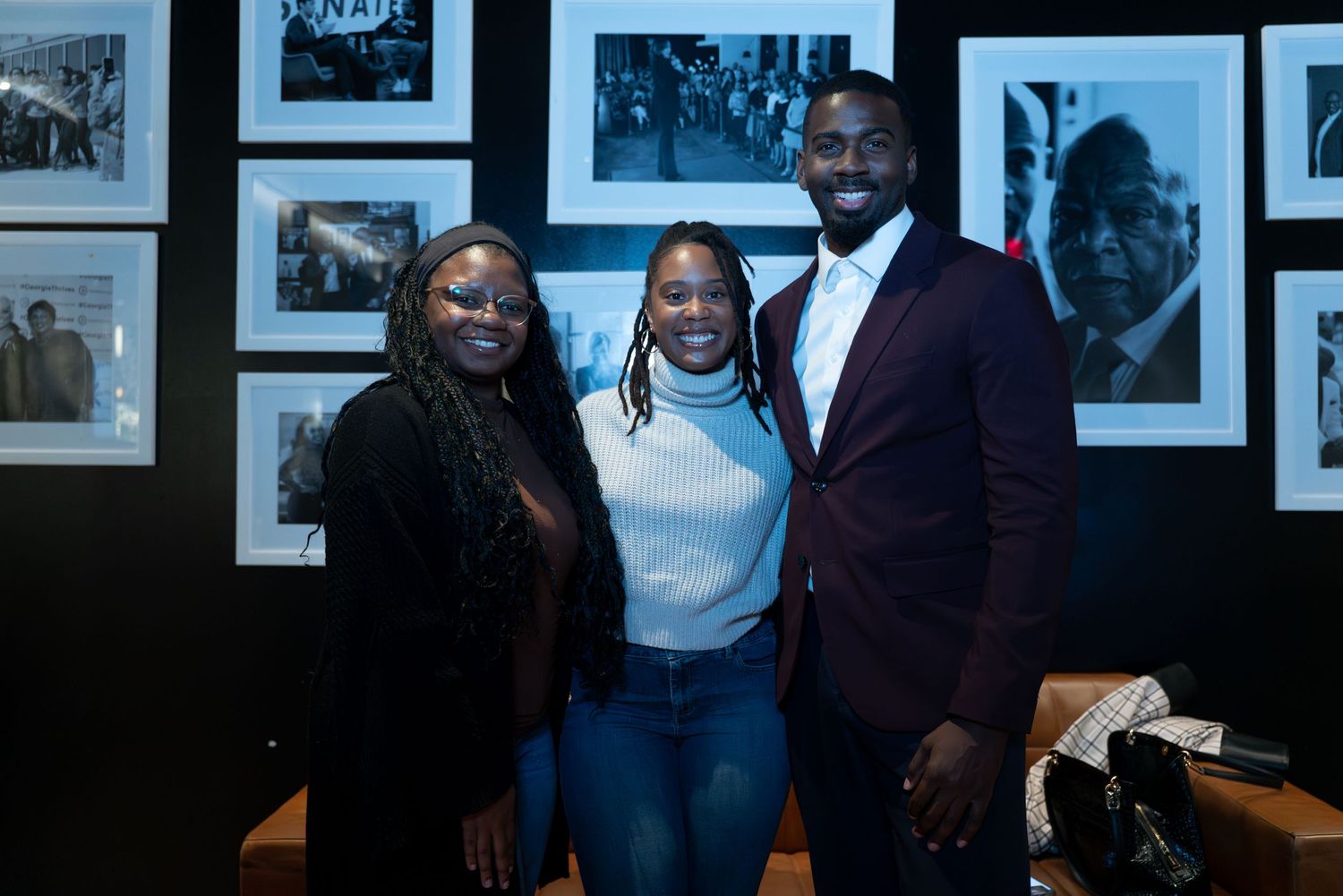 A group of people pose together in front of a wall of black and white photographs in a gallery setting.