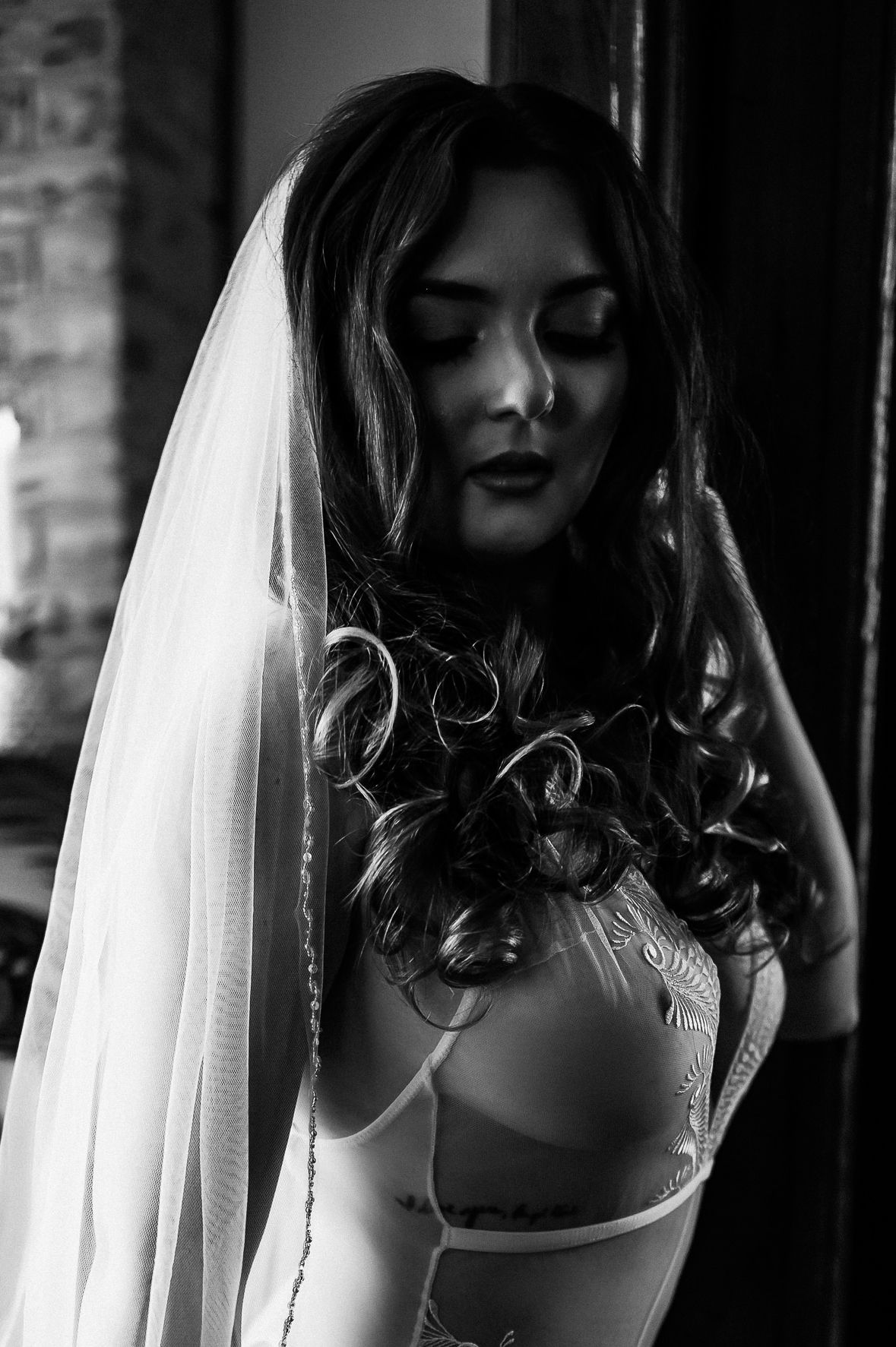 Black and white portrait of a bride wearing a veil and white dress, eyes closed, with curly dark hair.