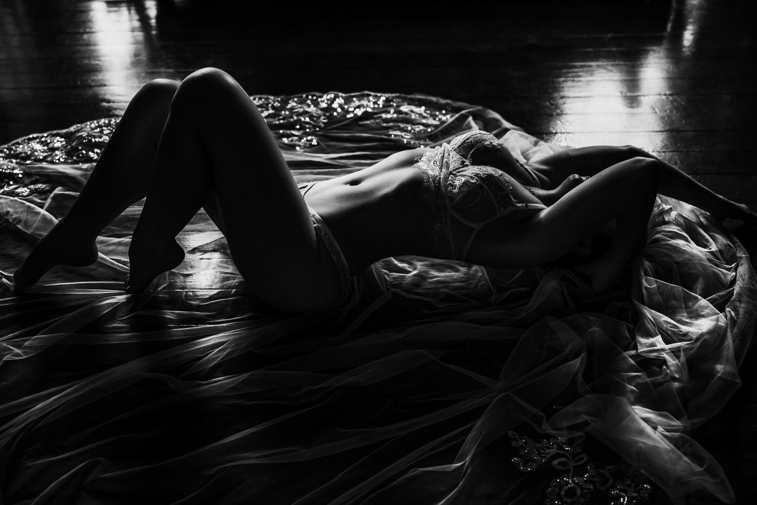 Black and white boudoir photo of a woman reclining on flowing fabric in dramatic low-key lighting. luxury bridal boudoir session