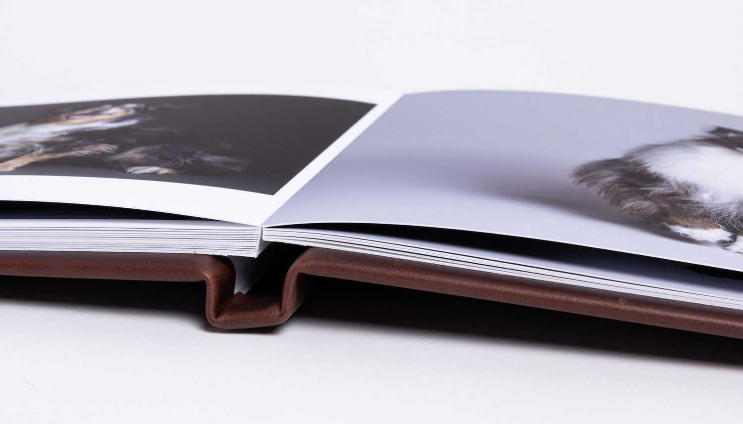 Open hardcover photo book with glossy pages displaying black and white photography, lying flat on white surface.