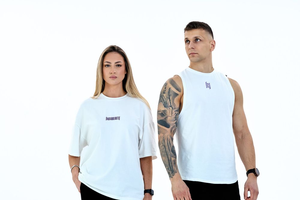 A man and woman wearing white oversized t-shirts and muscle tank tops against a white background.