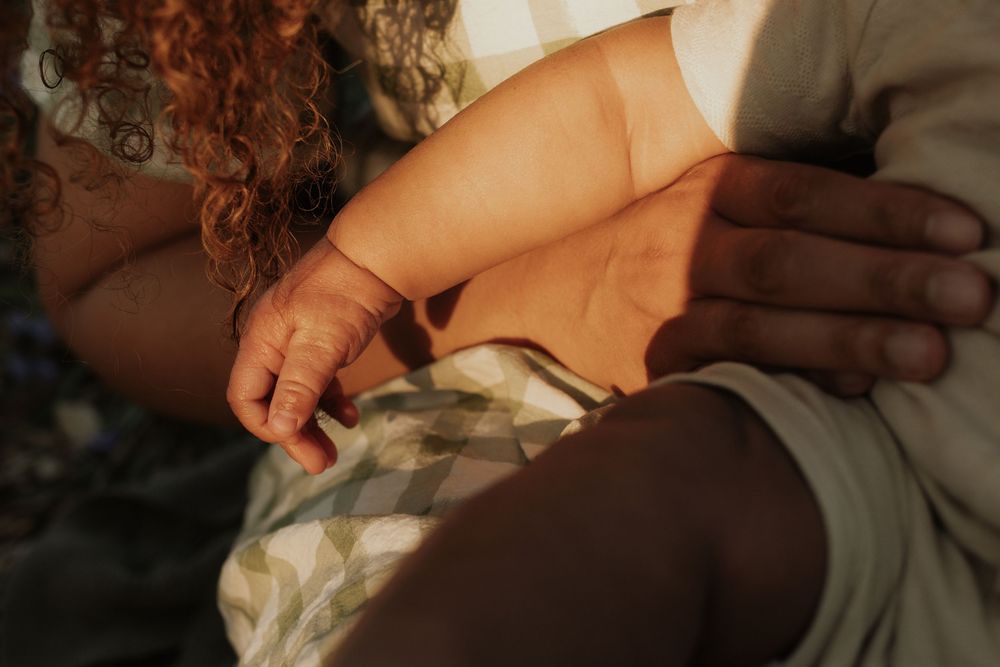 Close-up of baby hand resting on mother's hand in warm sunset light outdoors.